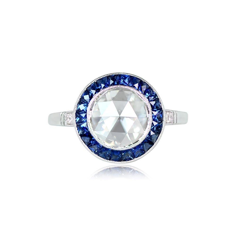 This engagement ring boasts a bezel-set rose-cut diamond center stone surrounded by a halo of French-cut calibre natural sapphires, totaling approximately 0.88 carats. The center diamond weighs about 1.56 carats, with K color and VS2 clarity.