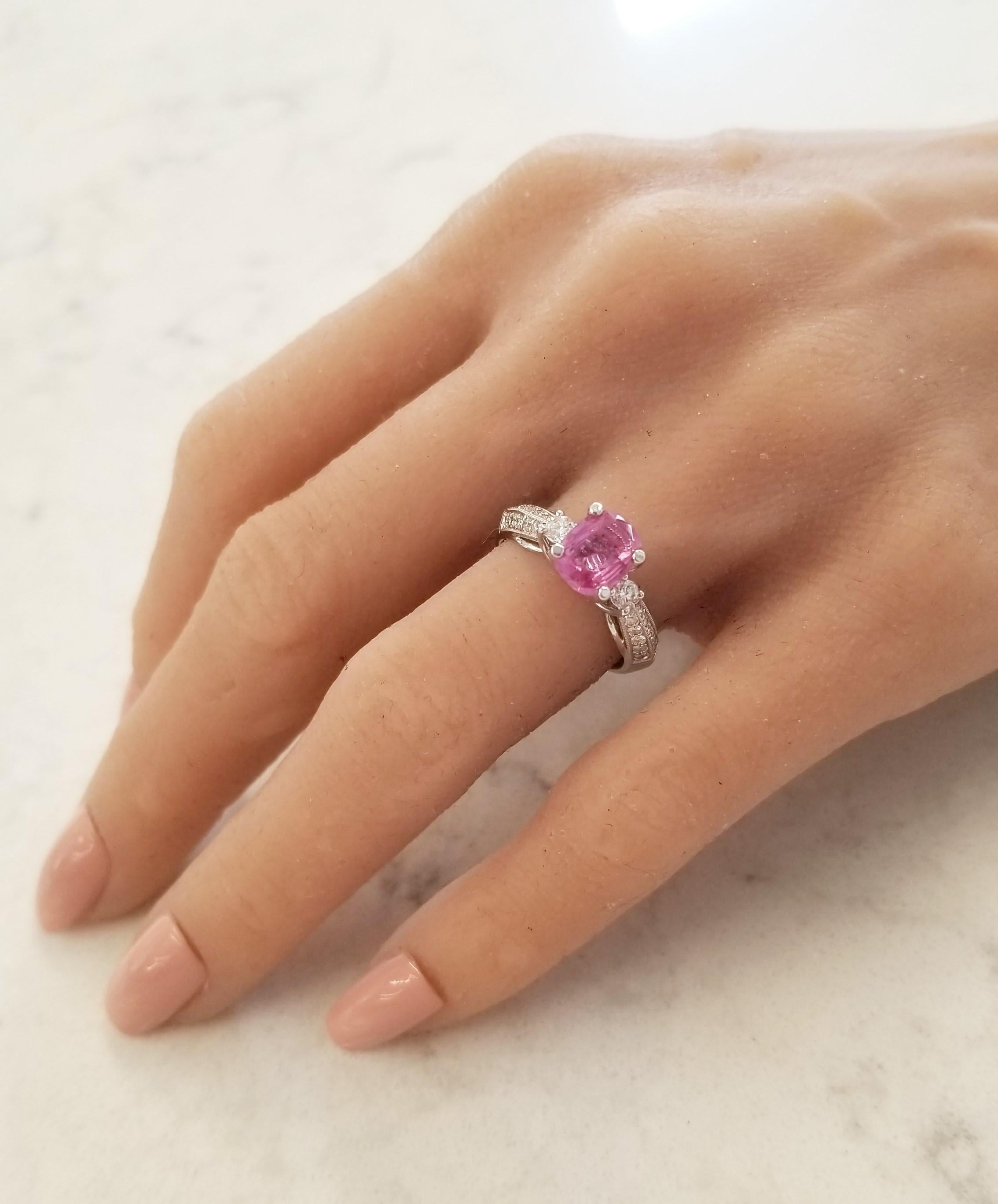 This striking piece features a shimmering 1.57 carat oval pink sapphire set into a secure four prong mounting. Its origin is Sri Lanka, its color is intense pink with excellent luster, transparency, and clarity. The sapphire has a brilliant round