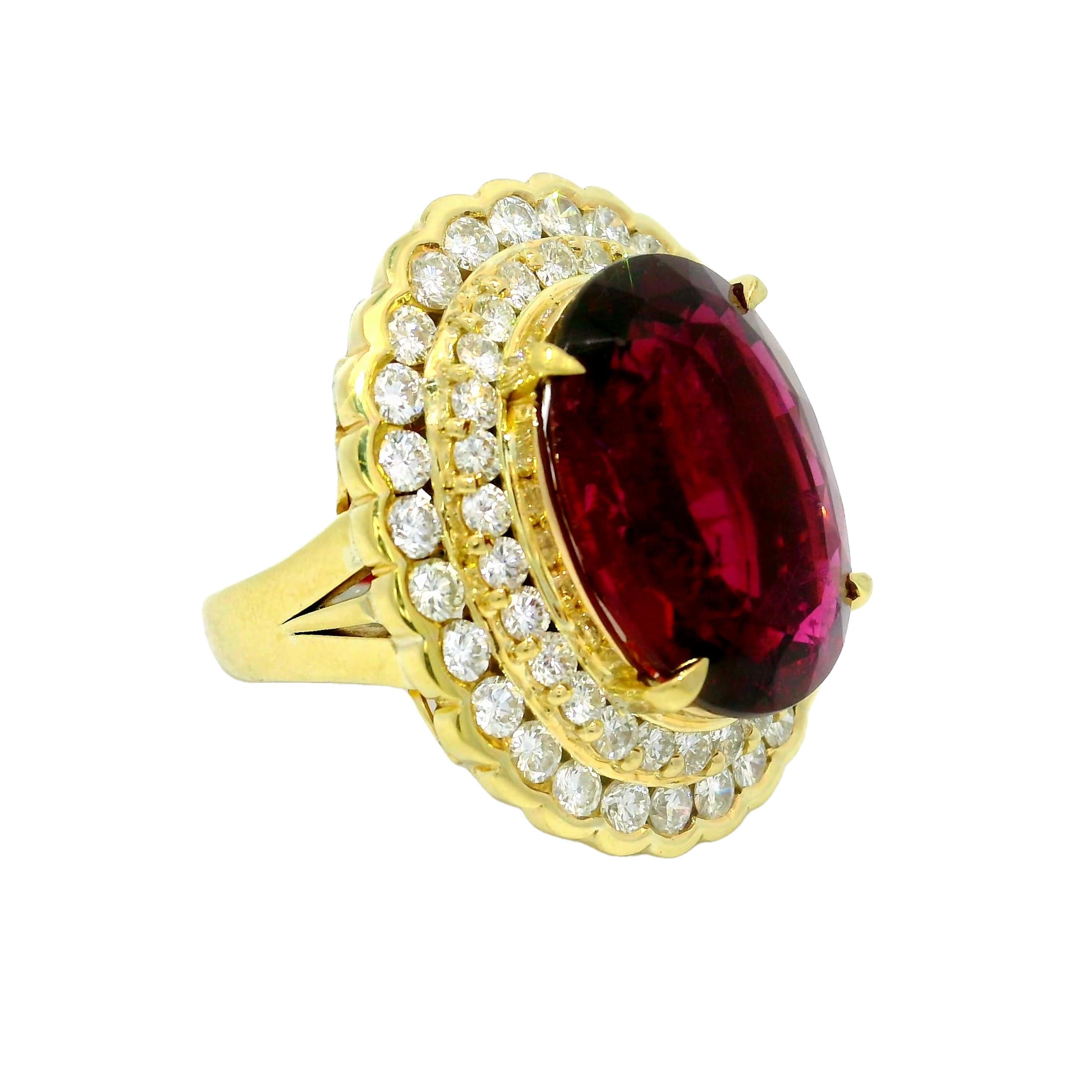 A contemporary fashion ring showcasing a 15.74 carat oval rubellite as its centerpiece. The rubellite displays a striking red hue, surrounded by 2.57 carats of round white diamonds, adding brilliance. Crafted in 18k yellow gold, this piece embodies
