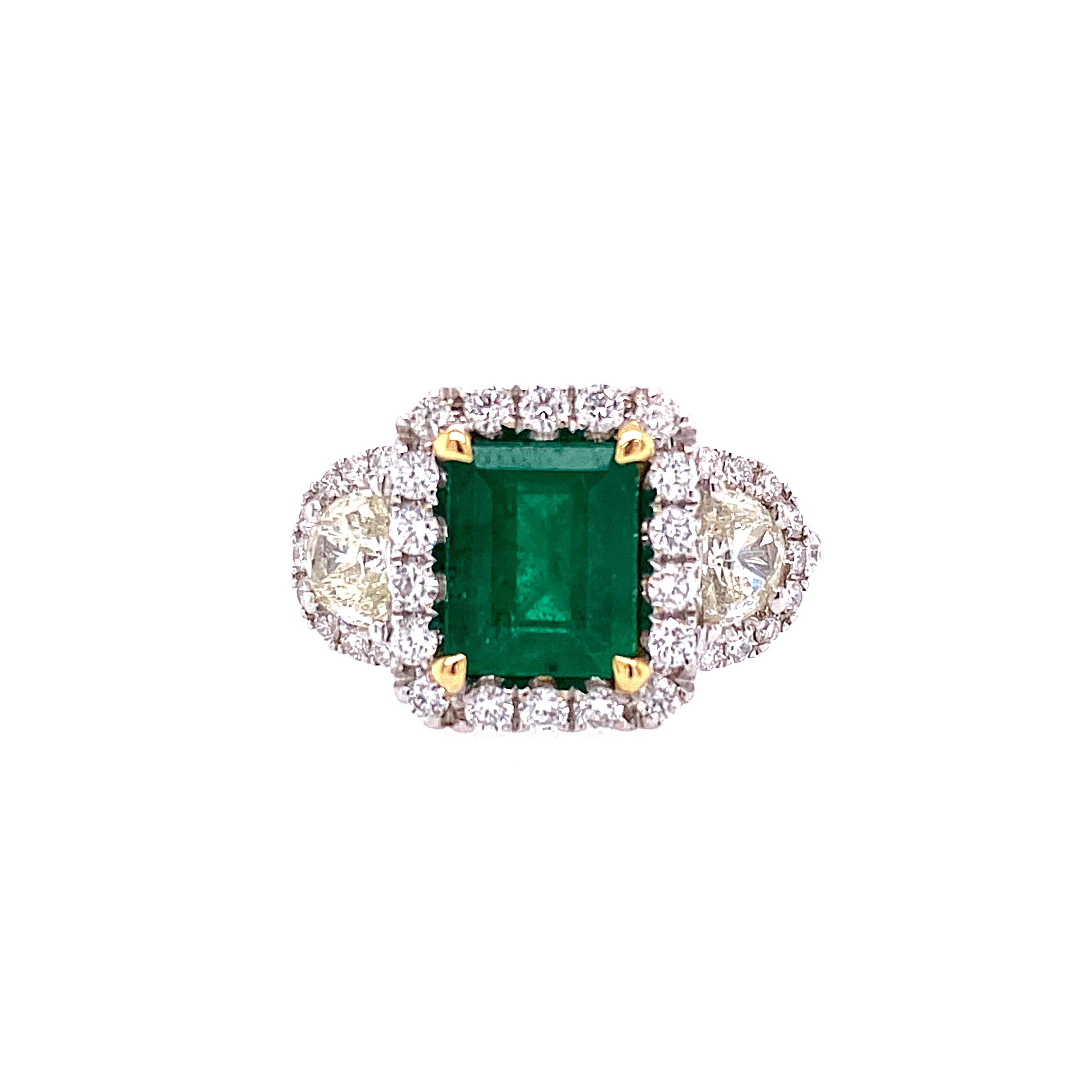 This stunning Cocktail Ring features a beautiful 1.58 Carat Emerald Cut Emerald with a Diamond Halo, on a Half Diamond Shank. The Emerald is flanked by a Half Moon Diamond on both sides. This Ring is set in 18K White Gold, with 18K Yellow Gold