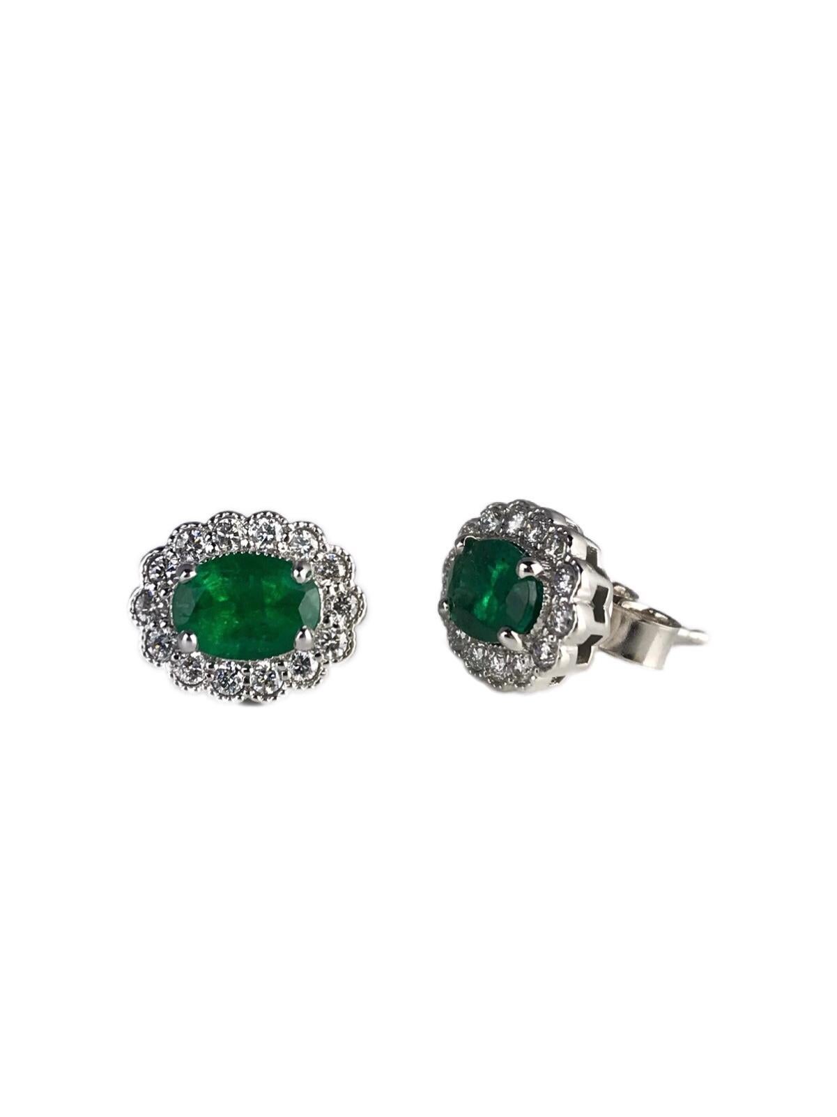 Presenting these exquisite earrings with oval-cut emerald centers, each elegantly encircled by a halo of round, natural diamonds. The intricate milgrain detailing in the setting infuses a timeless, classic allure. The emeralds, in their 7x5mm oval