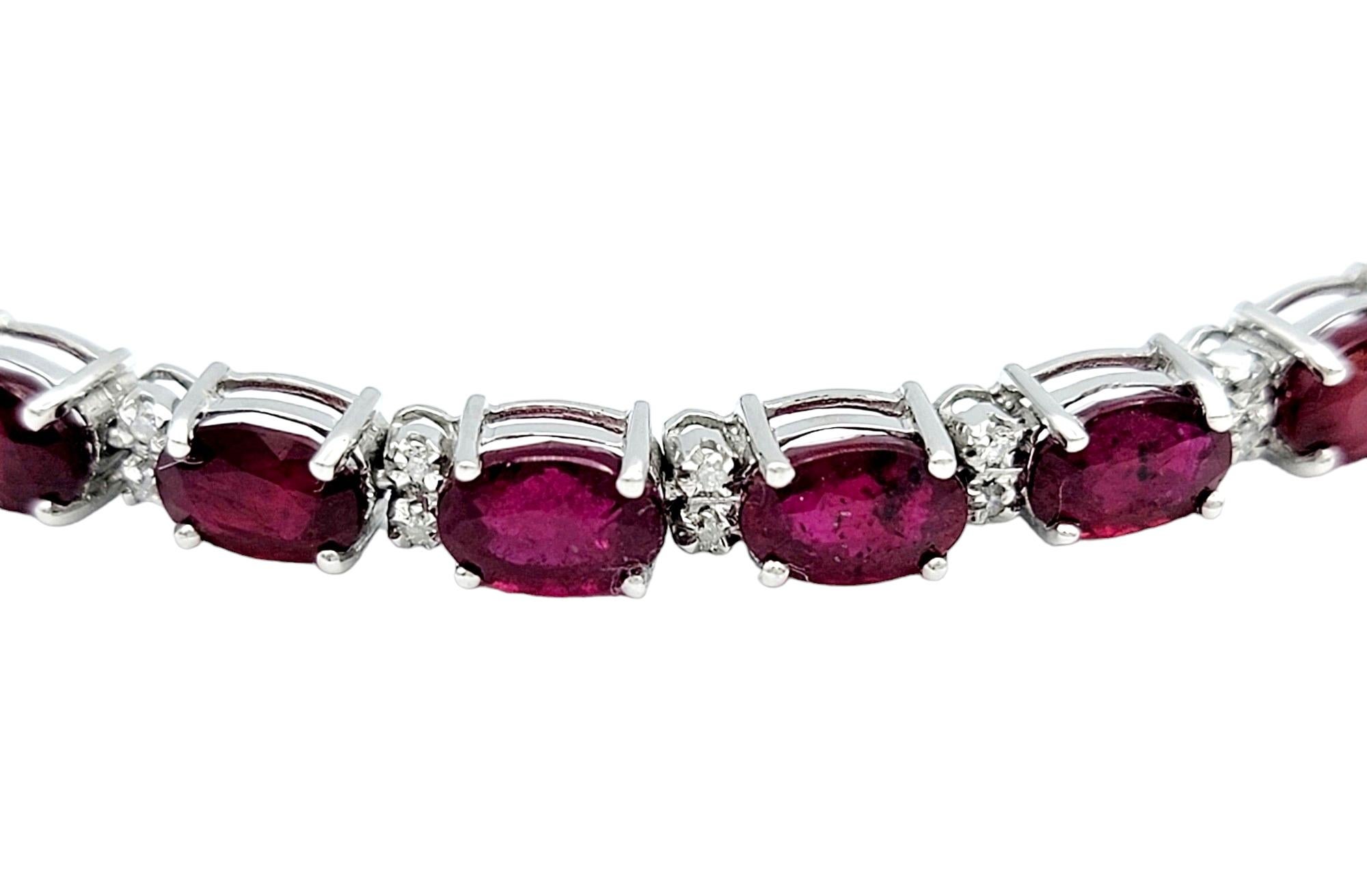 This exquisite allure of this ruby and diamond tennis bracelet, a harmonious symphony of gemstones set in the timeless embrace of 14 karat white gold, is sure to impress. The alternating arrangement of horizontal-set oval rubies and round diamonds