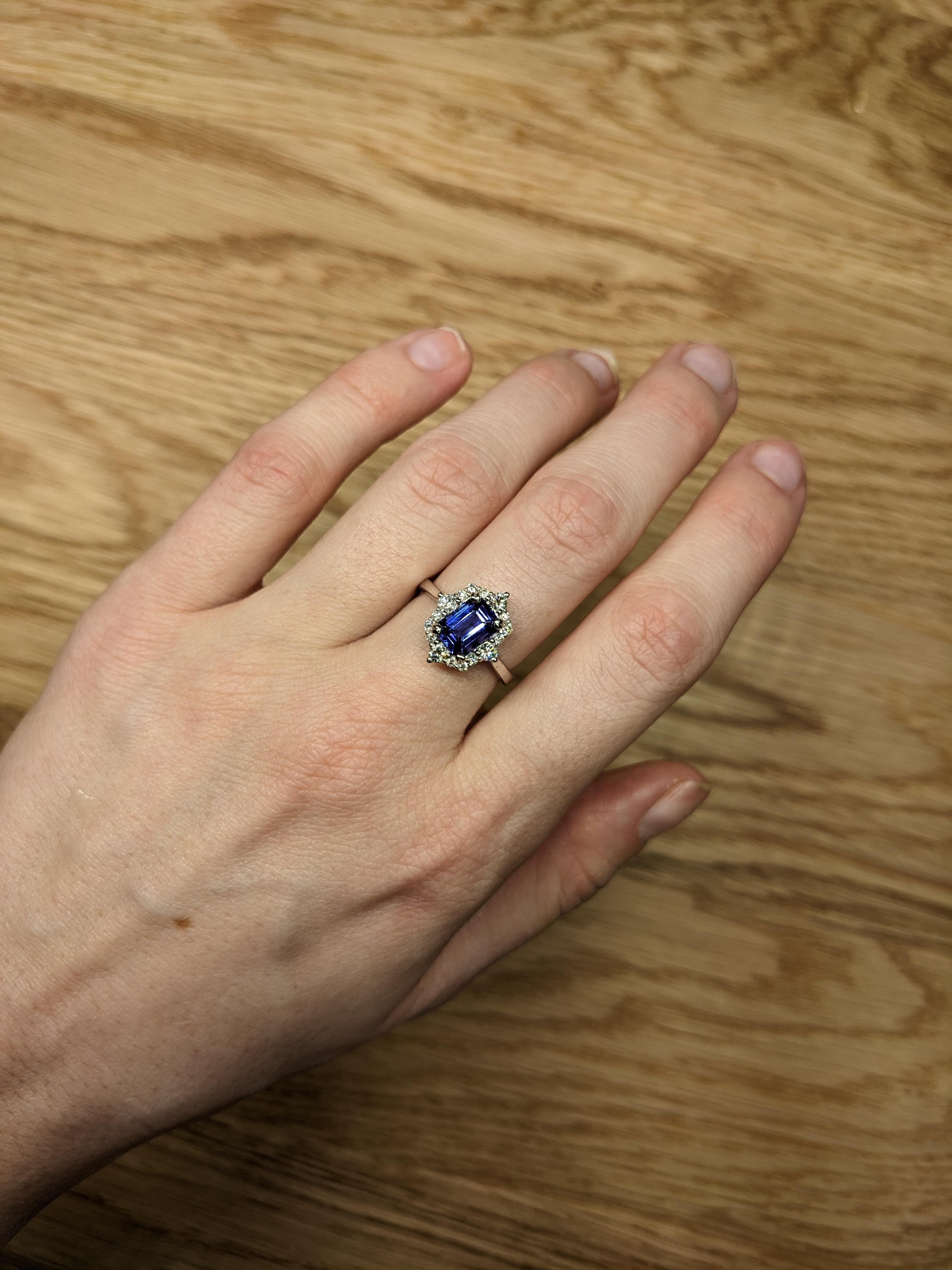 A beautiful ring features a striking tanzanite stone with an emerald cut, known for its rich blue-violet color. The diamonds surrounding the tanzanite add extra brilliance, making it a luxurious and elegant piece of jewelry. The 14K white gold