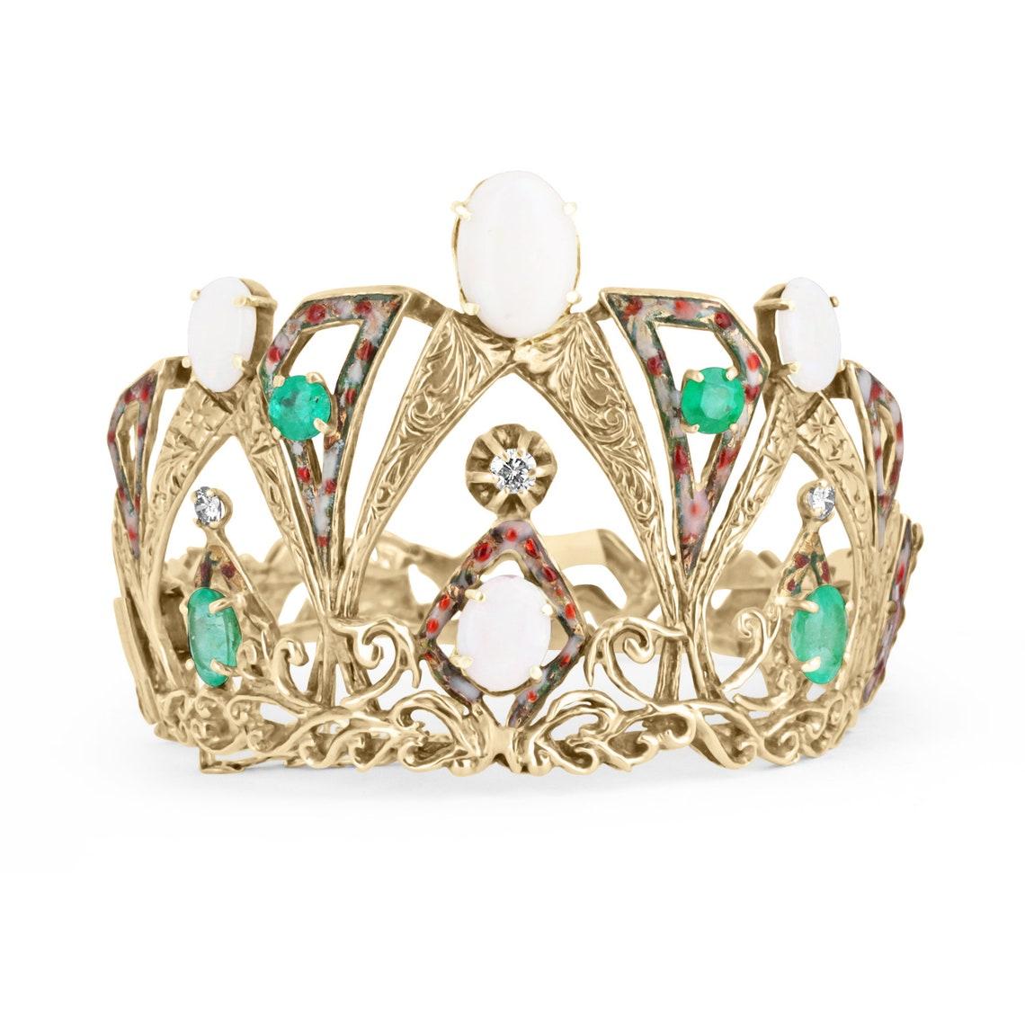 Showcased is a vintage emerald, diamond, and opal filigree crown bangle. This exquisite piece features four natural Colombian emeralds with a total weight of 5.38-carats and four dazzling white opals with a total weight of 10.05-carats. The piece