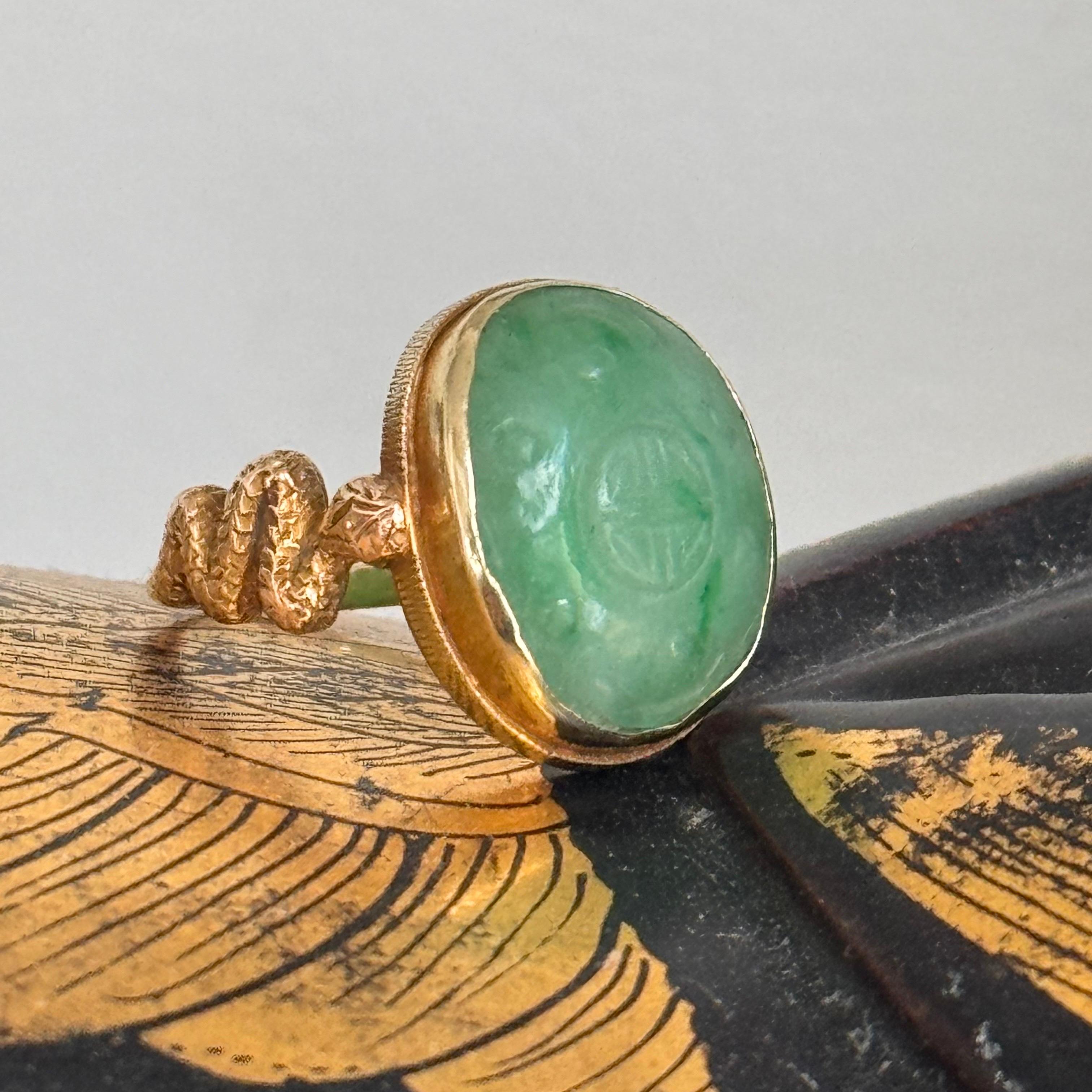 Cette bague vintage exquise présente un anneau en or jaune 15 carats, élégamment conçu avec un pendentif en jade ovale serti d'un chaton. Le jade est orné d'un personnage central sculpté, ce qui en fait le point central de la pièce. Le jade est