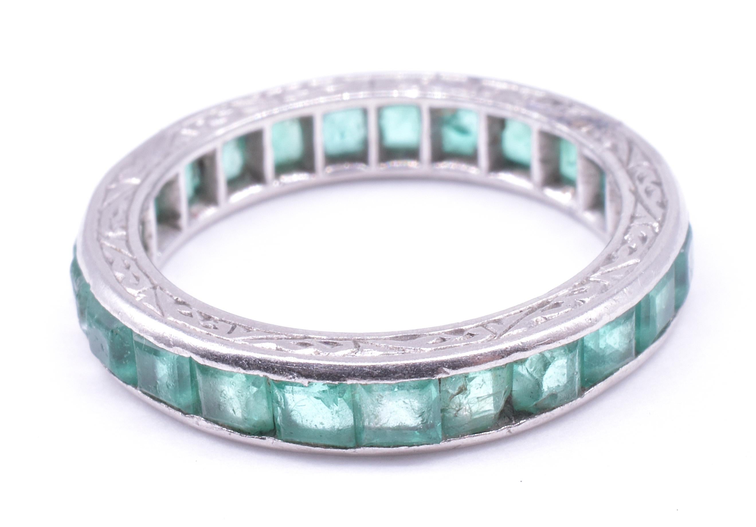 Our Deco emerald eternity band is crafted with an engraved 15K white gold band which with decorative flourishes and lines all along the rim and features 24 clear green emeralds with a total carat weight of 1.15 carats. The inside of the band has