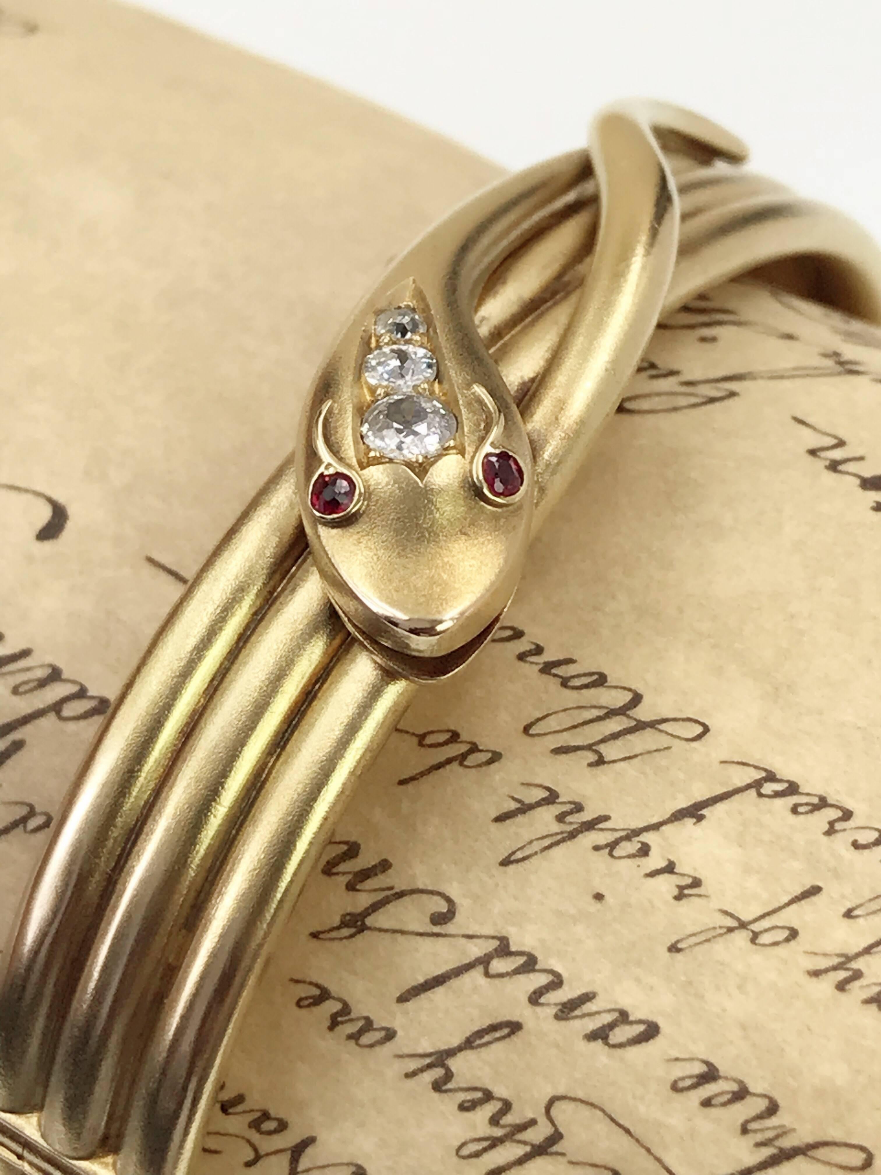 A late Victorian 15ct gold diamond snake hinged bangle. Designed as a coiled snake, with old-cut diamond line crest and red-gem eyes. Estimated total diamond weight 0.30ct, H-I colour, P1 clarity. Inner diameter 6cms. Weight 18.9gms. 