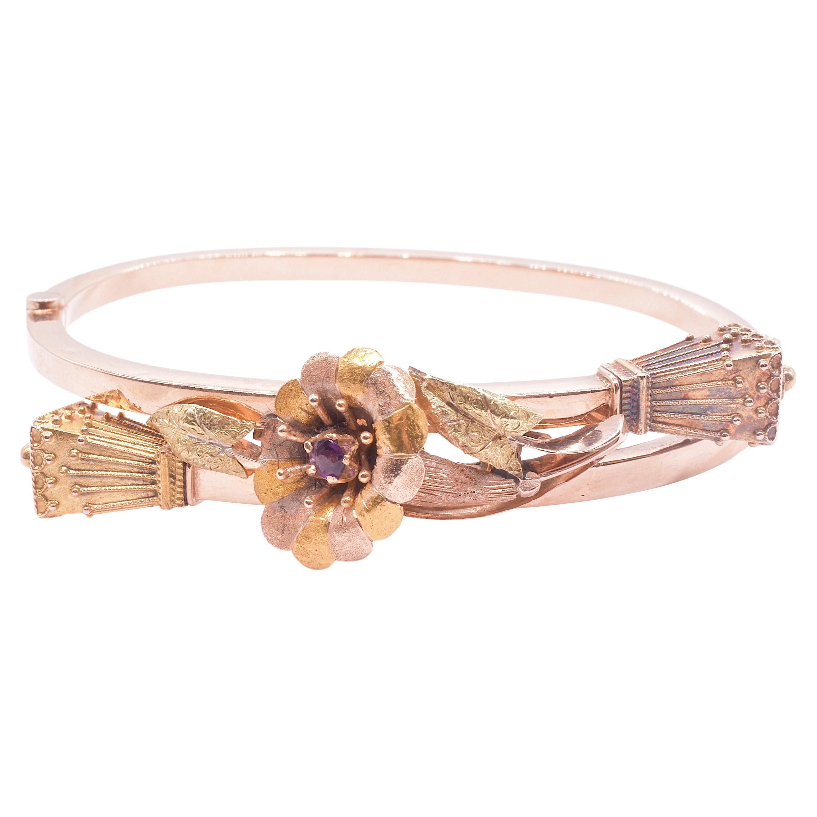 This two-color gold articulated hinged bracelet is capped with lantern finials and a 2 color gold pansy with leaves springing forth in between the finials. We love the ornamental detail; the leaves have alternating gold colors and a garnet at the