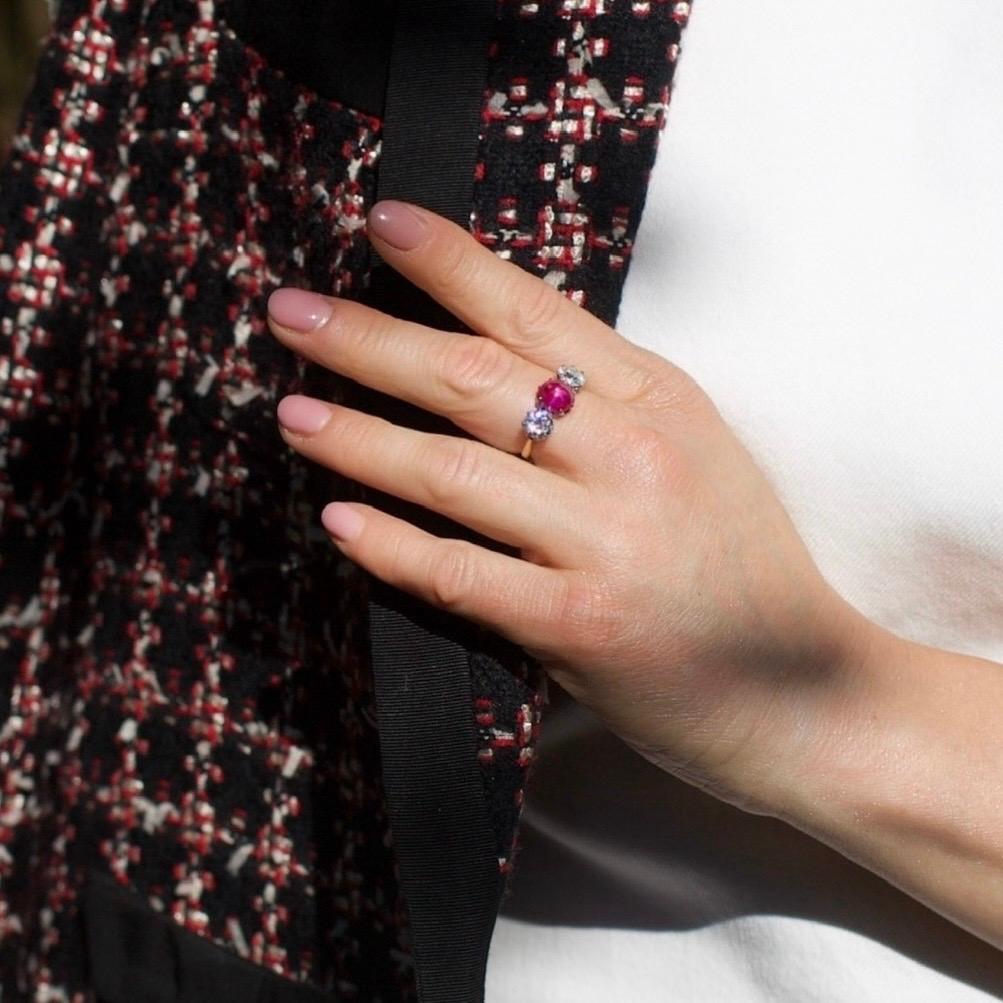 An antique three-stone ring crafted in 15kt gold with platinum settings, centring on a natural cabochon ruby of vivid pinkish-red colour. The ruby is mounted in a secure claw setting and flanked by two old European-cut diamonds of exceptional