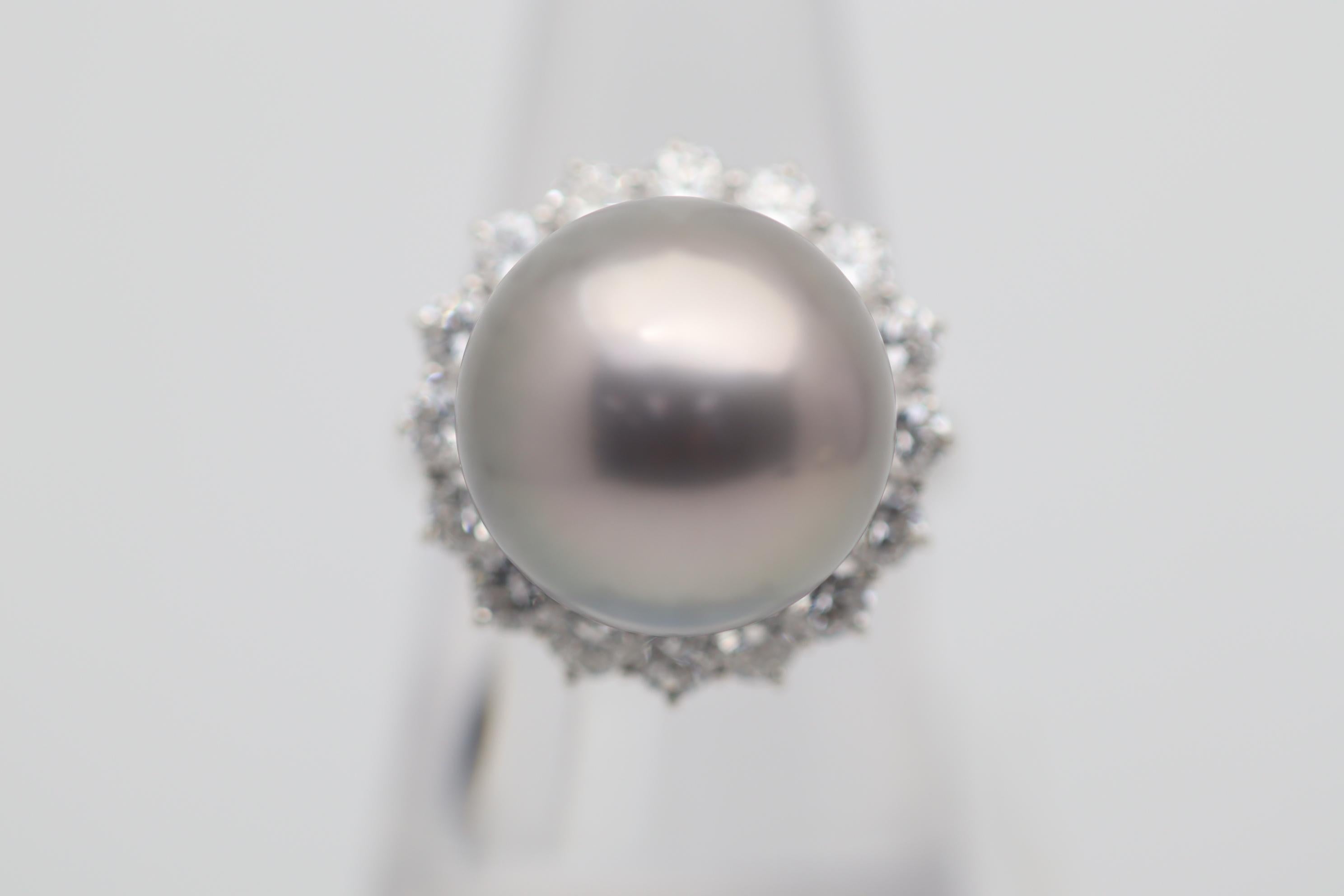 A fine Tahitian pearl measuring 15-millimeters takes center stage. It has a perfectly round shape along with an intense silver-gray color, fantastic nacre, strong luster, and a soft pink overtone. It is complemented by 1.76 carats of round