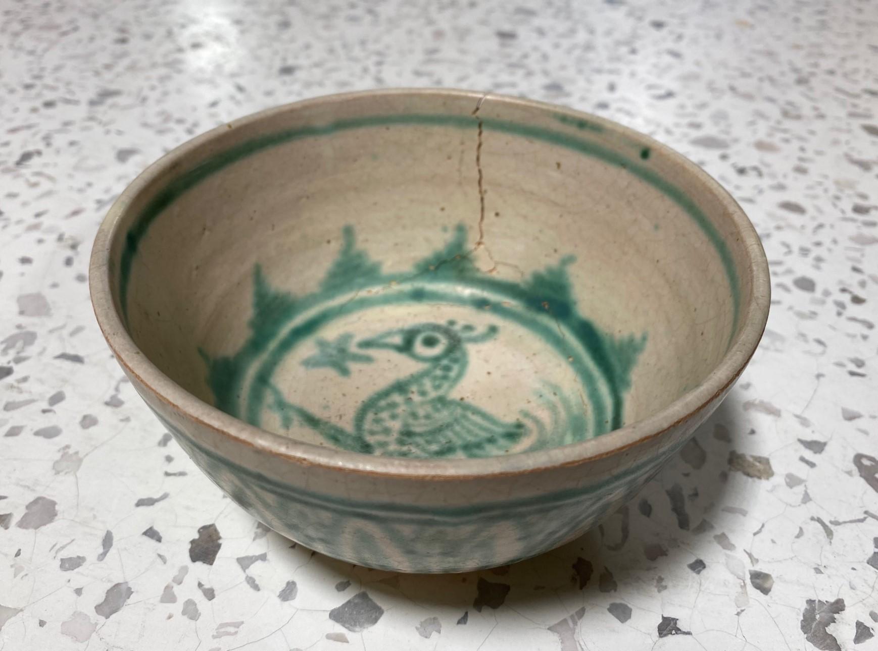 A beautiful and somewhat rare Burmese (Burma/Myanmar) 15th-century hand-painted and decorated green and white earthenware bowl. The piece is decorated with a bird in the center and has a stylized motif of green lotus petals painted against a