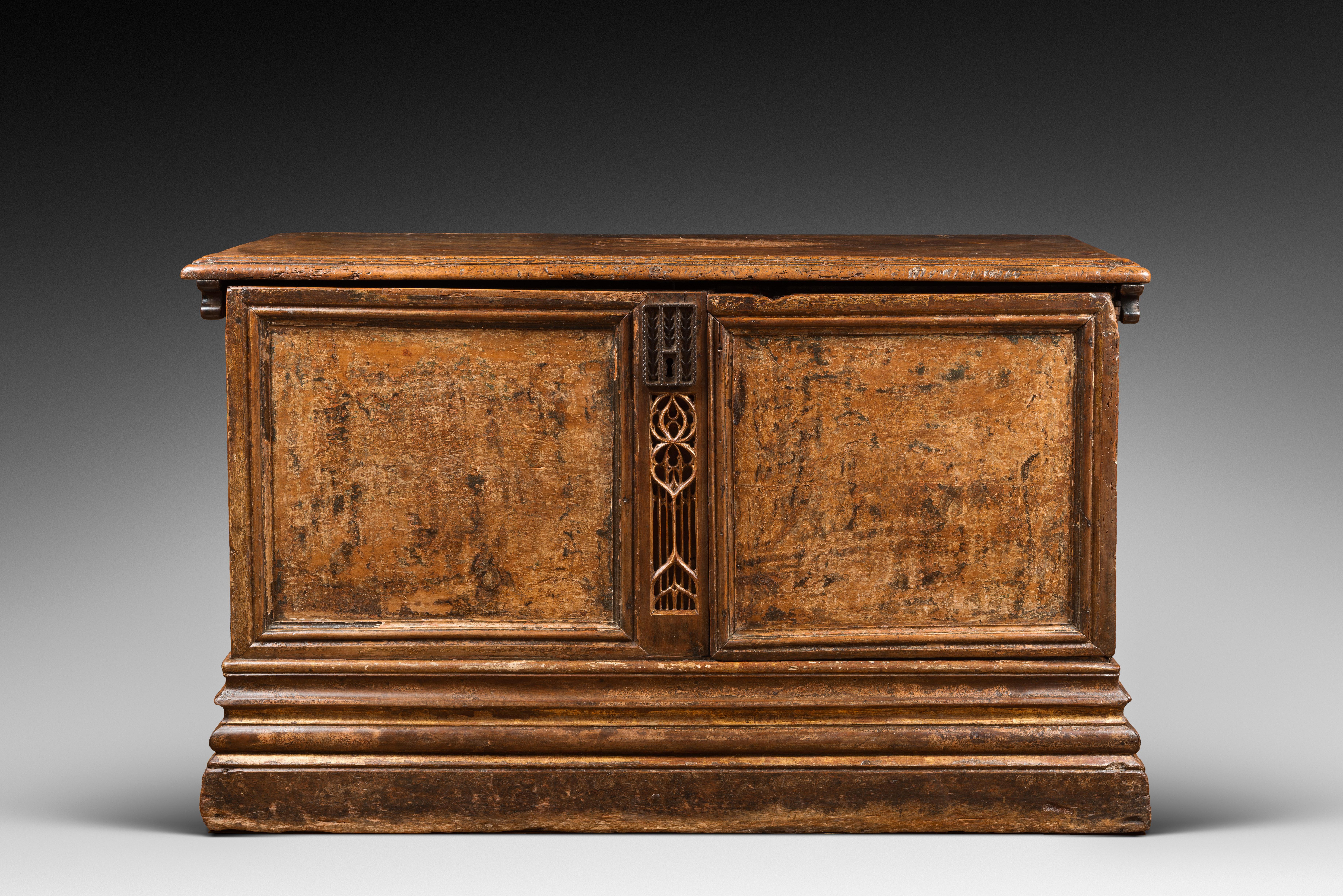 This chest stands on a high moulded plinth. It was made from a fine walnut wood and shows good traces of polychromy and gold leaf decor. 

The facade’s two panels, once colourful, are divided by a Gothic fenestration element. The lateral panels