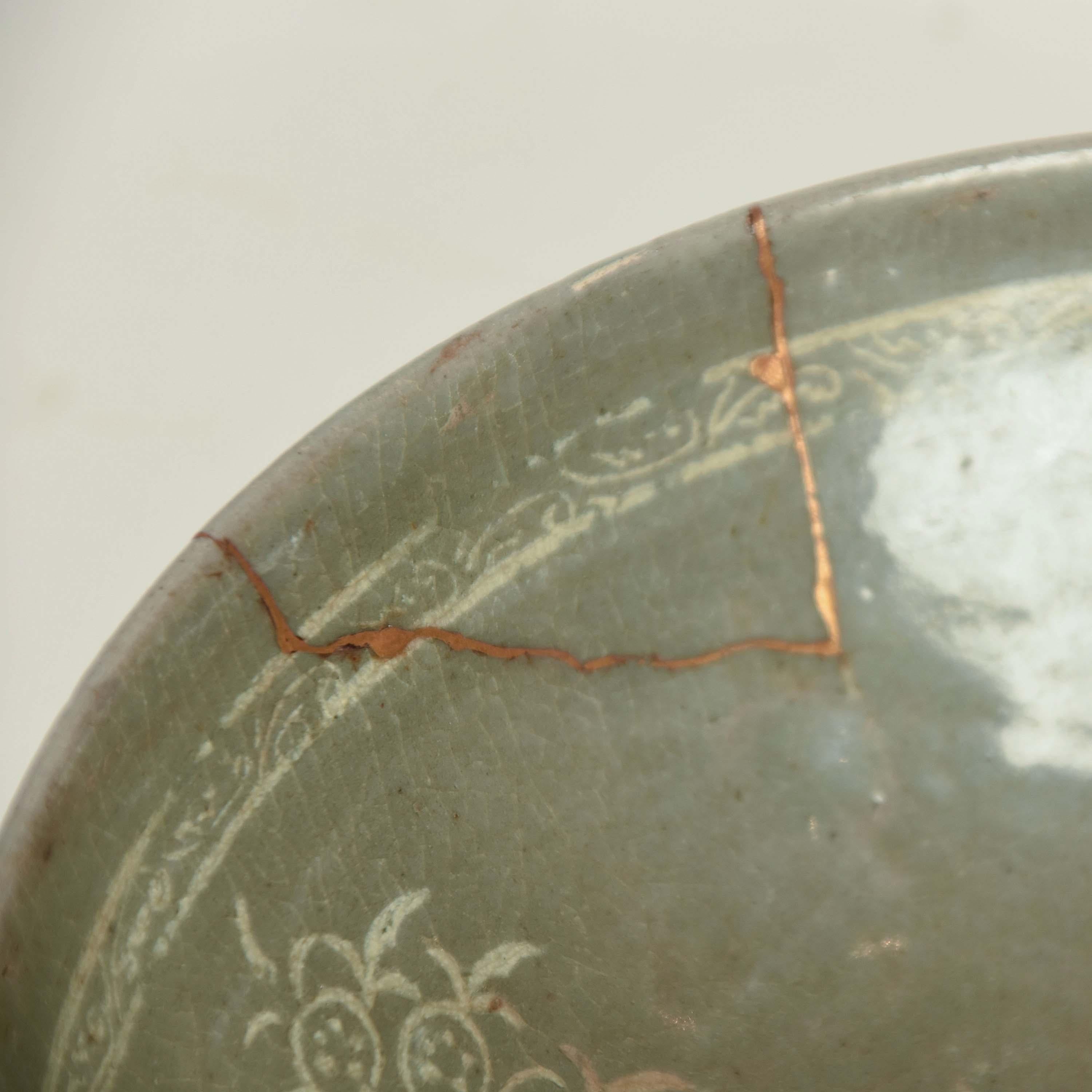 An antique Korean celadon glazed stoneware tea bowl from 15th century. It has been lovingly repaired with gold, using the kintsugi method, sometime during its long life, adding an extra layer of beauty and value. Kintsugi literally means 