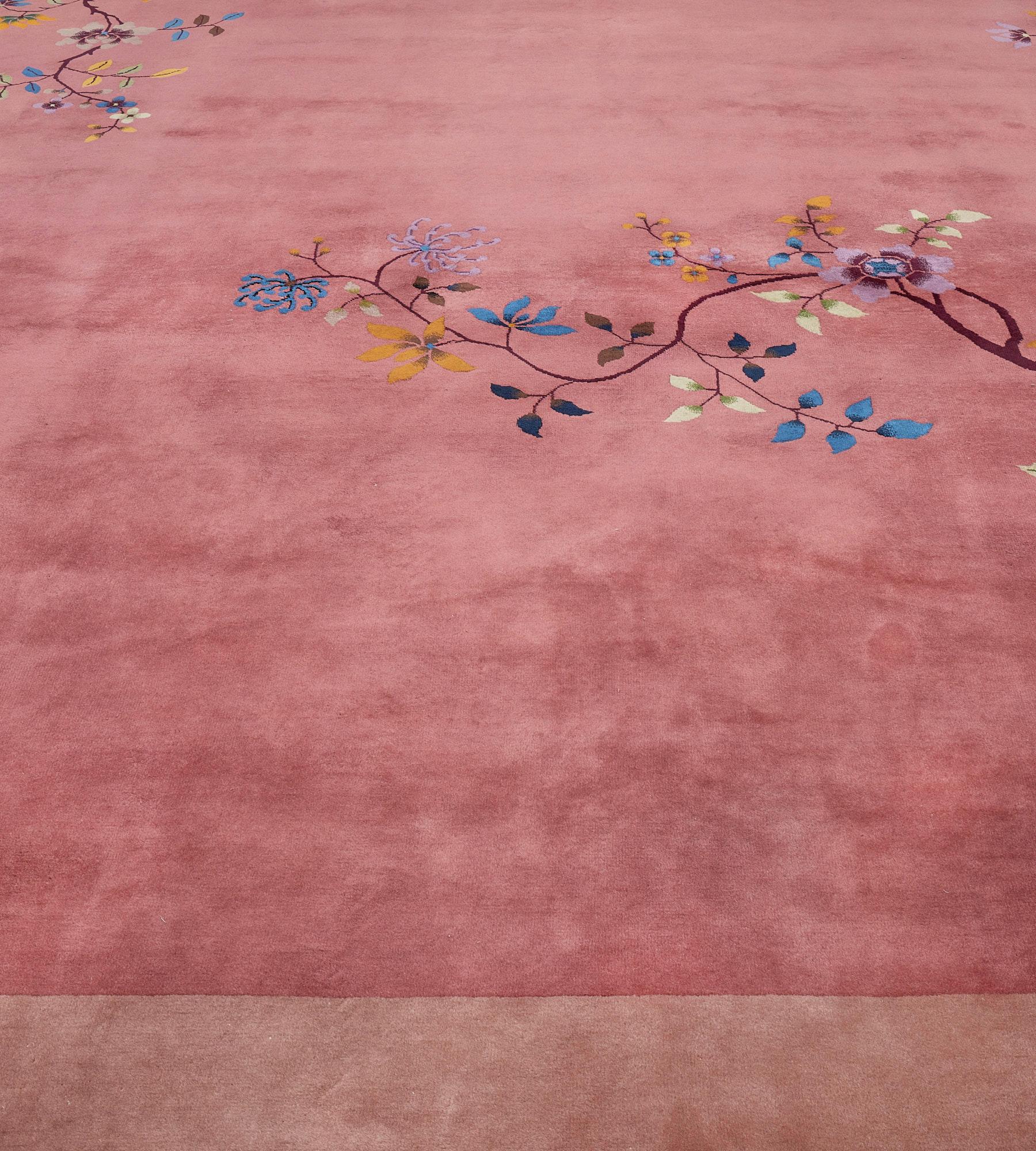 This antique, circa 1930, Chinese Peking rug features a dusty-pink field with delicate tendril flowering stems at each corner with auspicious symbols hanging from the branches, in a broad pale-pink border with stylized rock formations issuing a