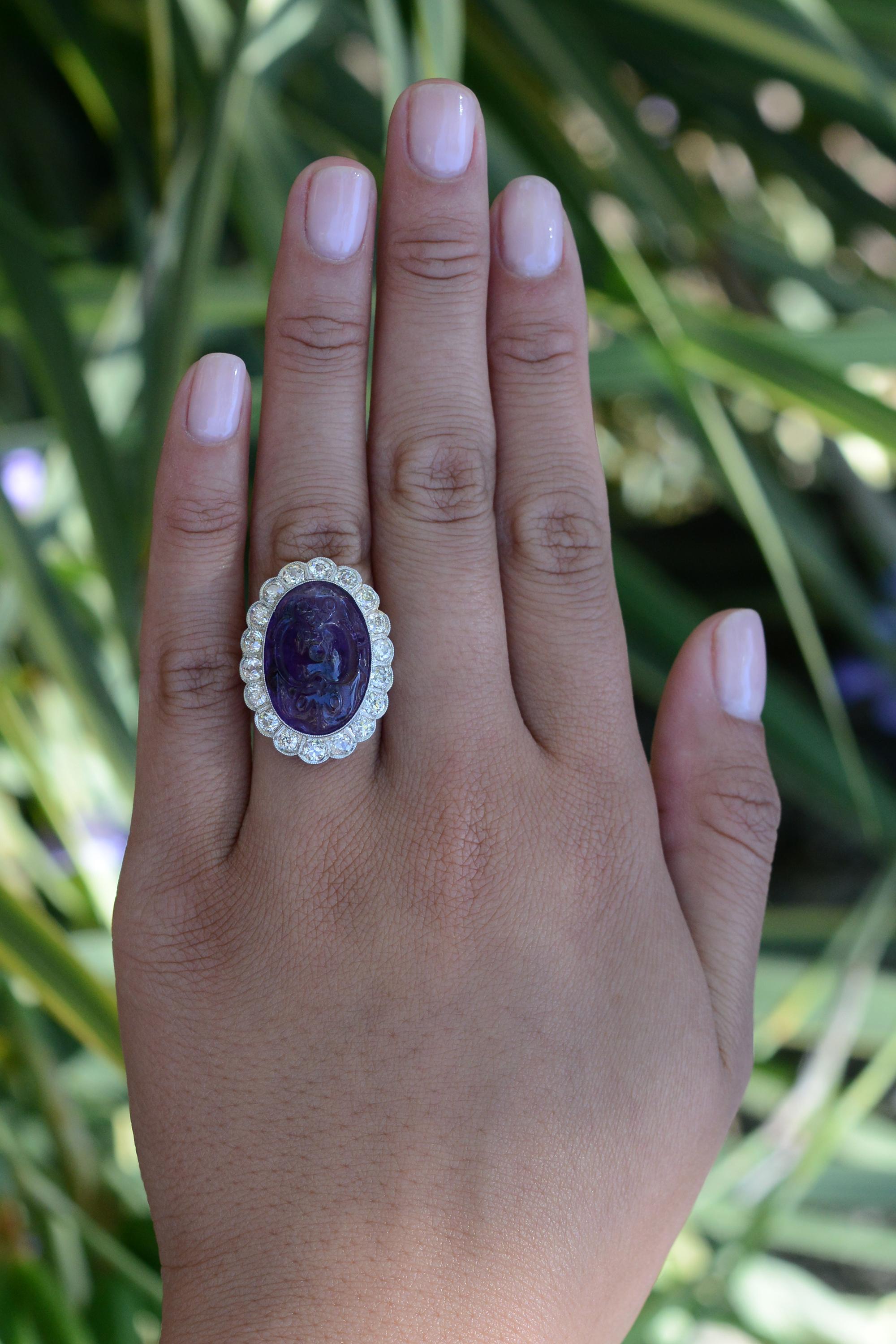 An exquisite vintage cocktail ring from the 1930s, concluding the grand Art Nouveau era. The centerpiece is a 16 carat amethyst, masterfully carved with two opposing bats, representing happiness. Gracing the gemstone is a scalloped halo adorned with