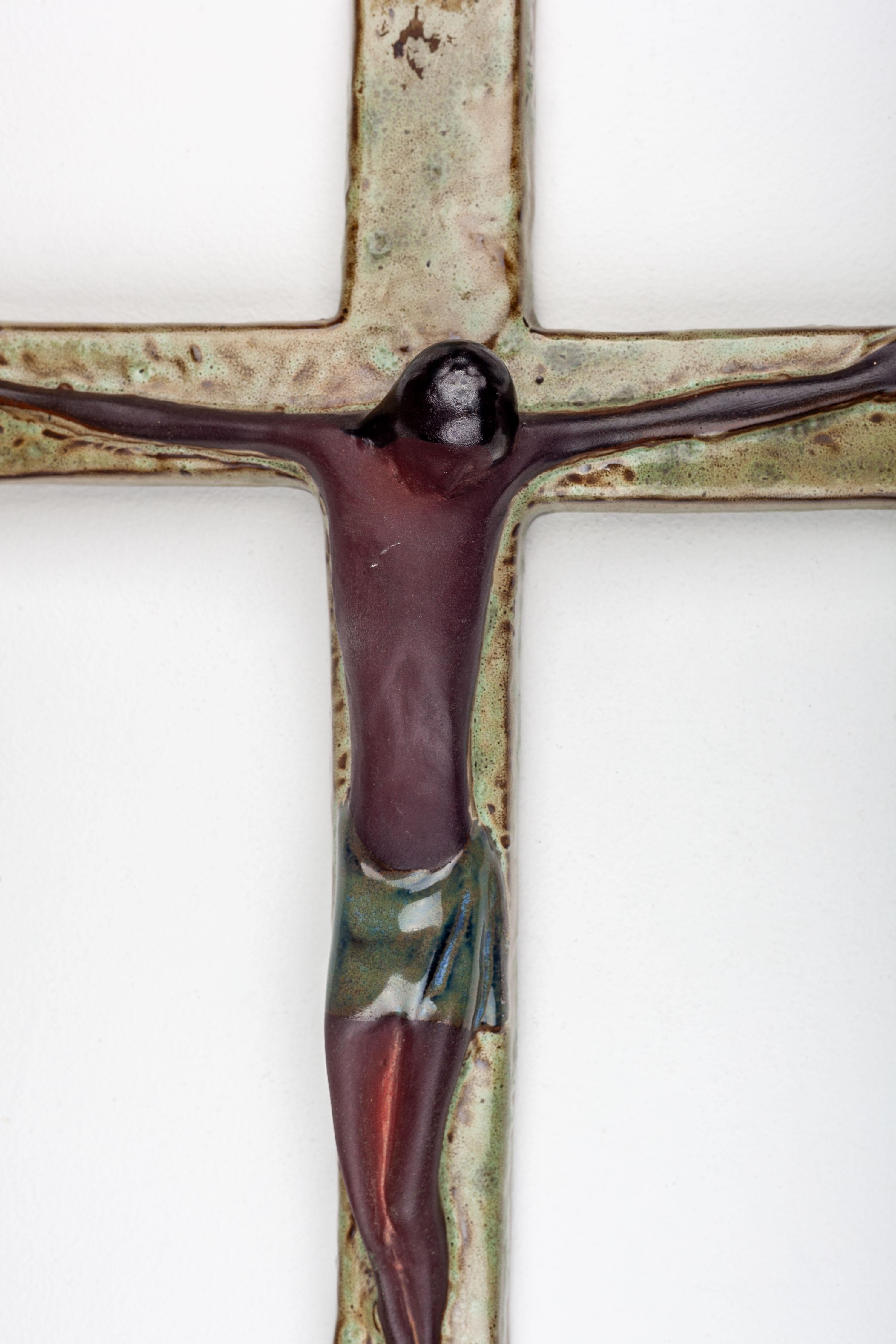 This 16-inch modernist studio pottery wall crucifix, meticulously crafted in Europe, showcases a unique design. It features a wall cross with chartreuse and brown moss-like texture, accompanied by a brown Jesus Christ figure.

The portrayal of