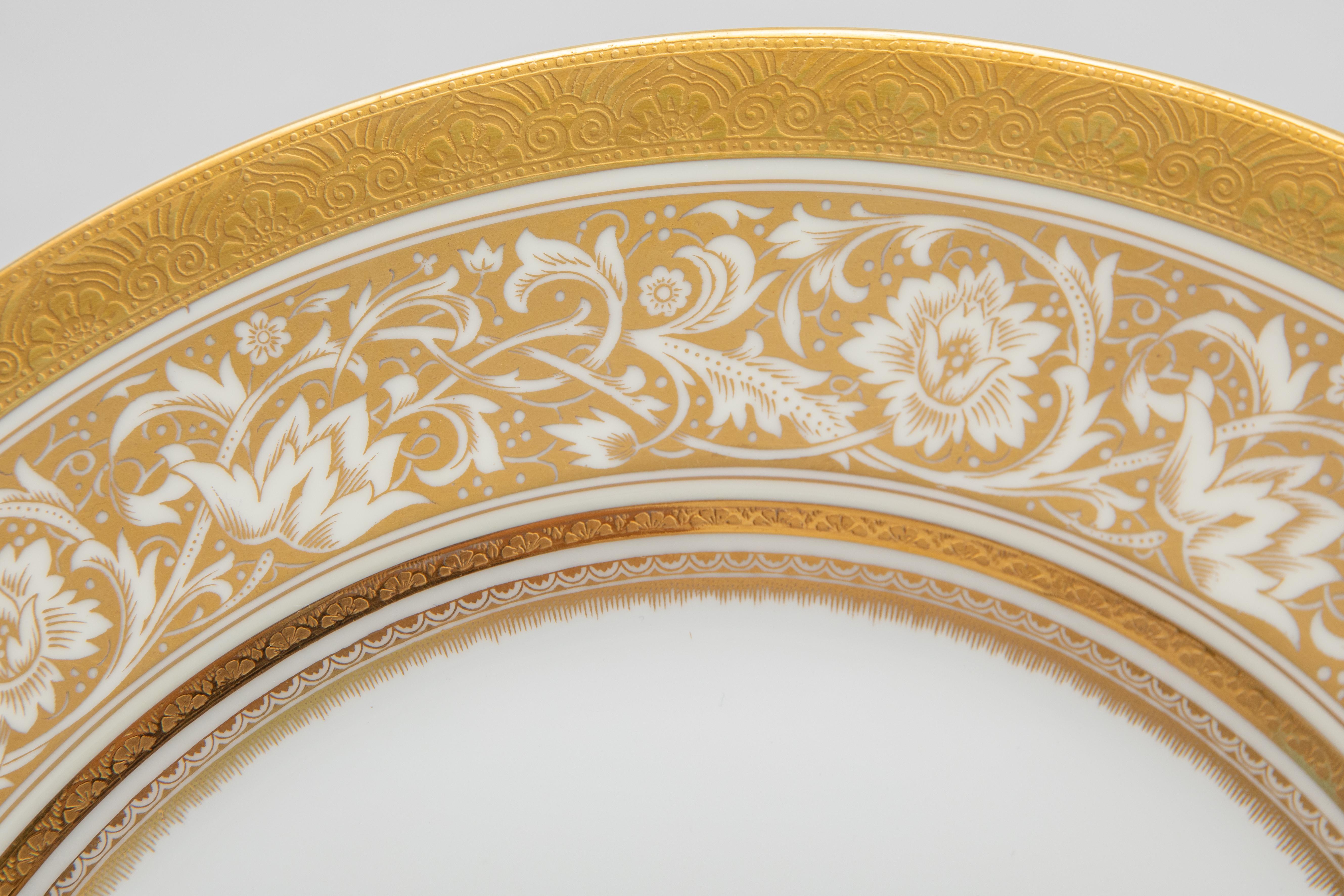Un classico ed elegante set di 16 piatti da portata di Minton, Inghilterra. Porcellana bianca e croccante con una doppia fascia dorata e un disegno floreale in oro 24 carati aggiuntivo sul colletto. Questo set vintage è in ottime condizioni ed è