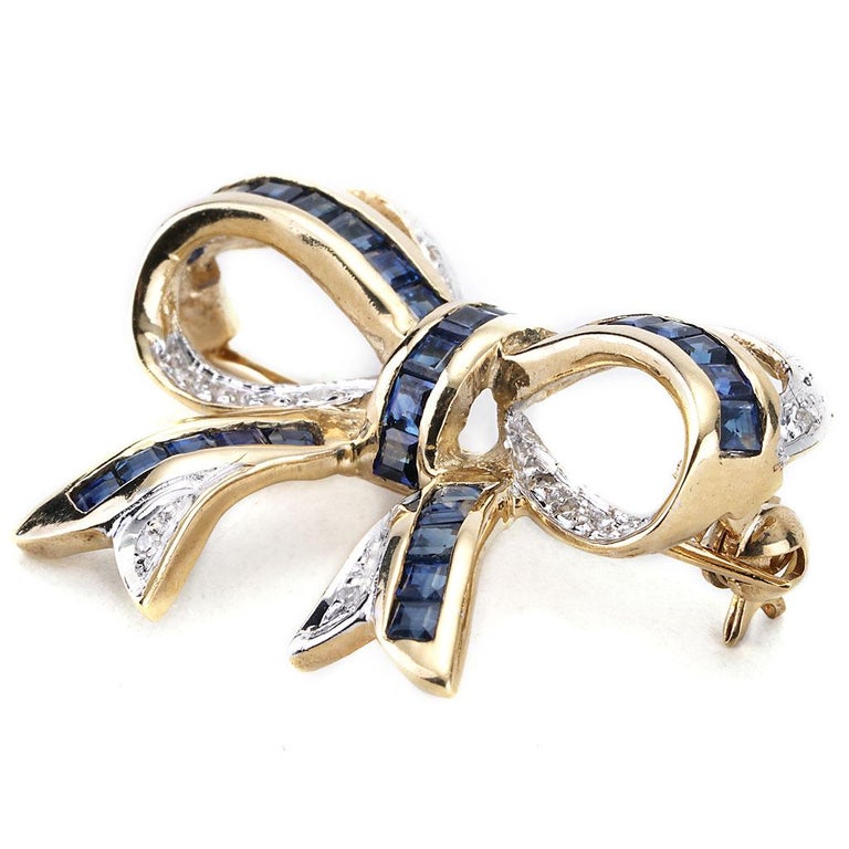 This antique sapphire and diamond bow pin is made of 14K yellow gold. It contains square sapphires weighing 1.50 CTTW, single cut I-J color and I1 clarity diamonds weighing 0.10 CTTW. 1 inch wide by .75 inches tall
