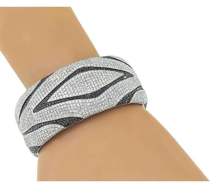 This is a stunning 18k white gold bangle. The bangle is set with sparkling round cut white and black diamonds that weigh approximately 16.00ct and 9.00ct respectively. The color of the white diamonds is G-H with VS clarity. The bangle measures 29mm