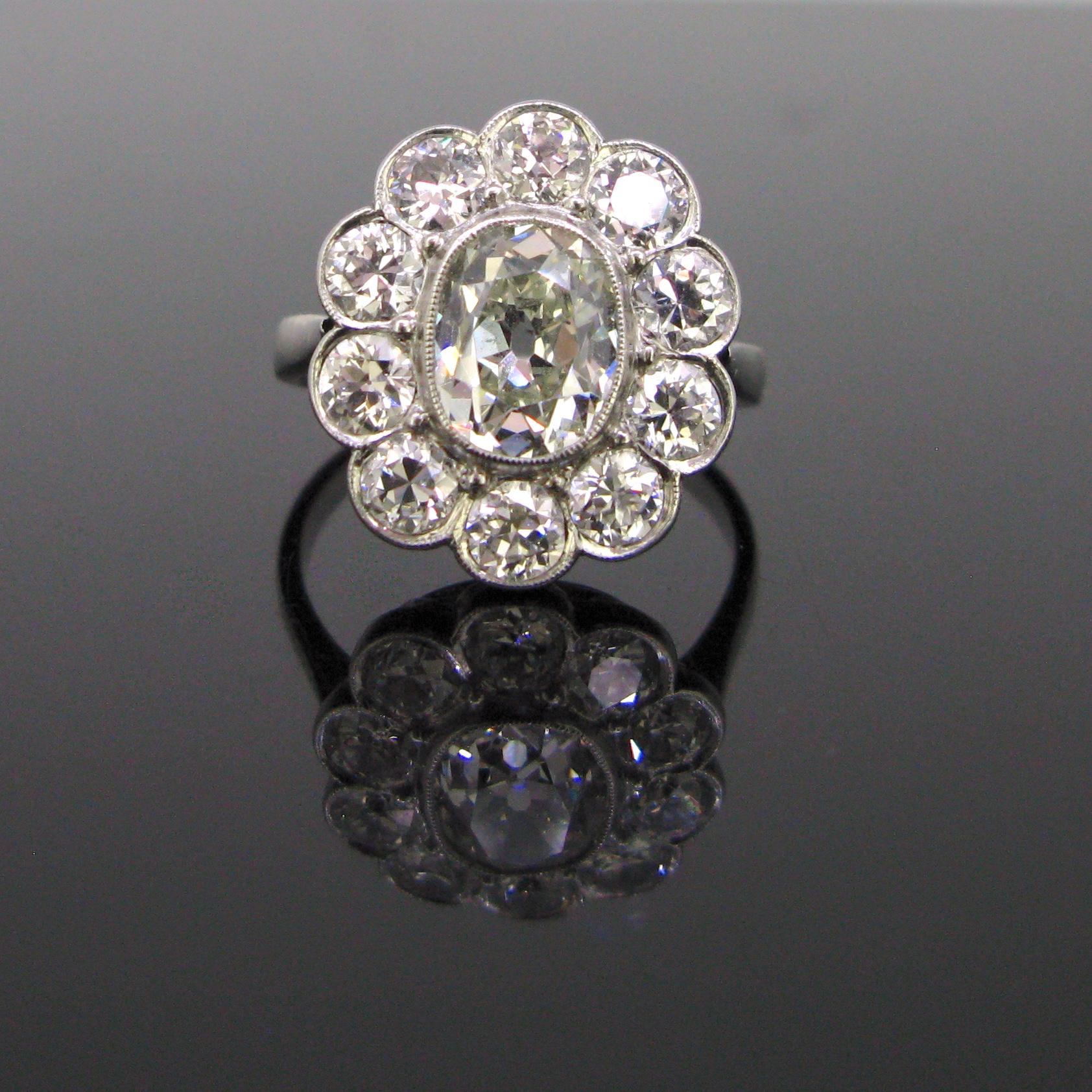 Comments: This beautiful Edwardian ring is fully made in platinum. It is set with a 1.60ct approximately oval cushion cut diamond surrounded with 10 old European cut diamonds. The total diamond carat weight is around 3.40ct. The ring has a very