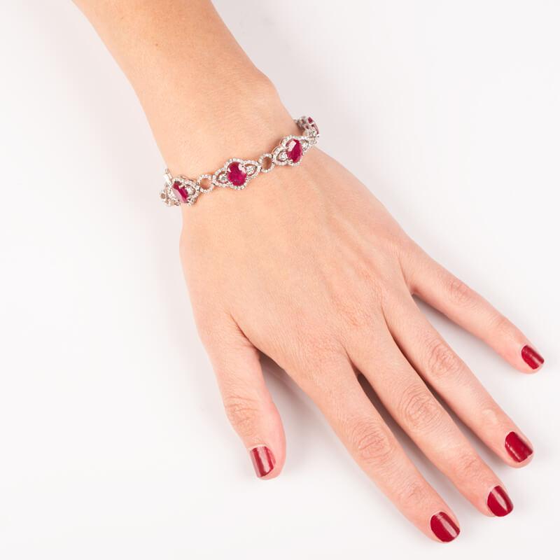 This beautiful bracelet features 16.10 carat total weight in oval cut natural rubies surrounded by 4.47 carat total weight in round brilliant cut diamonds linked together and set in 14 karat white gold. Box with safety clasp. It is approximately 7