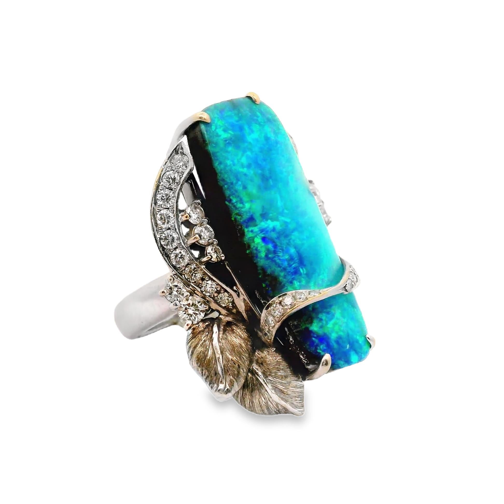 A large, beautiful, and impressive Australian boulder opal takes center stage. It weighs a substantial 16.39 carats and has excellent play-of-color as strong vibrant flashes of various green and blue colors dance across the stone. It is complemented