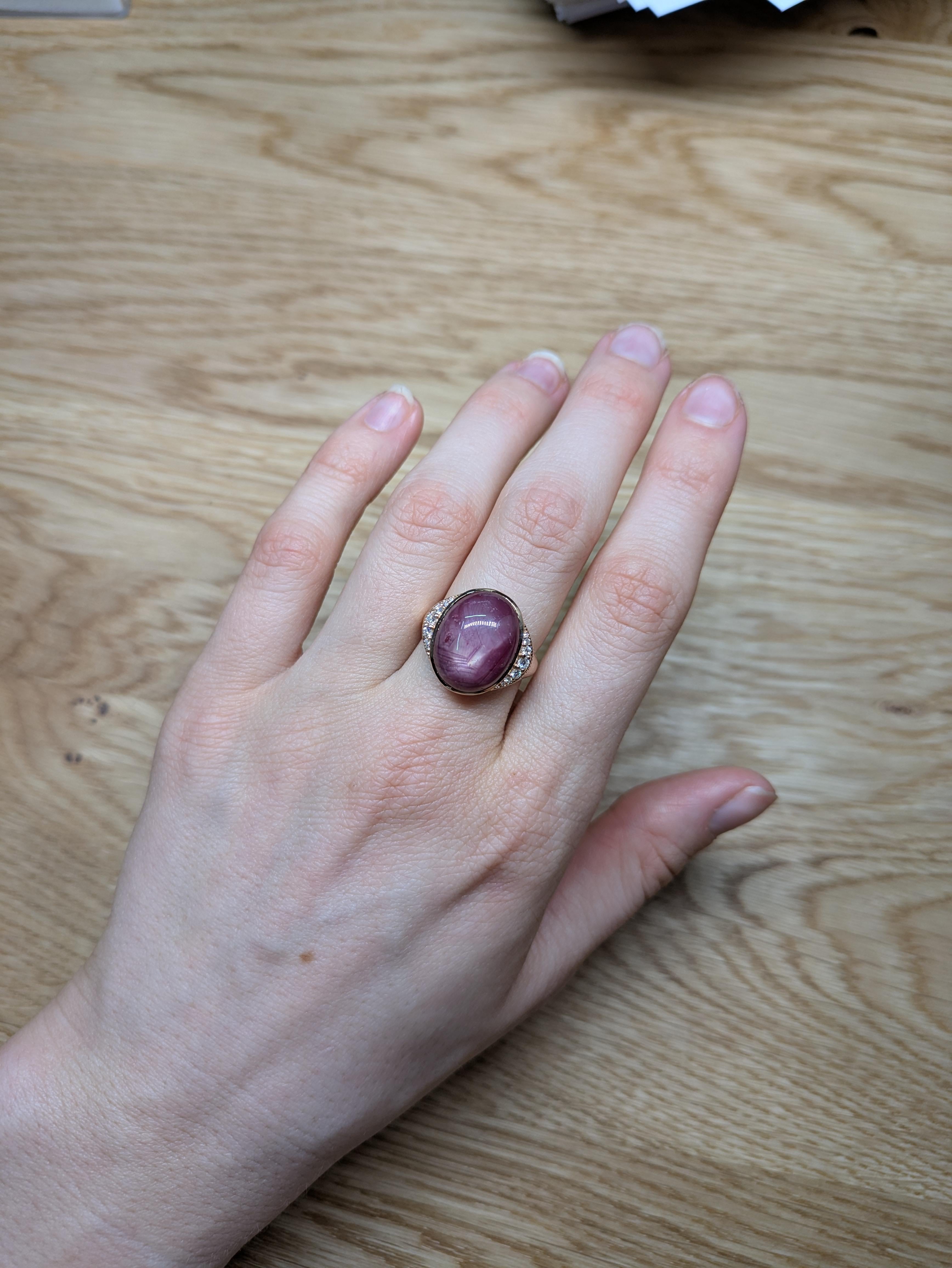 This statement ring showcases a stunning 16.28 carat oval Star Ruby gemstone, flanked by natural earth mined diamonds on each side. The setting is crafted in a solid 14K gold band, exuding a bold and luxurious charm. This Star Ruby ring makes a