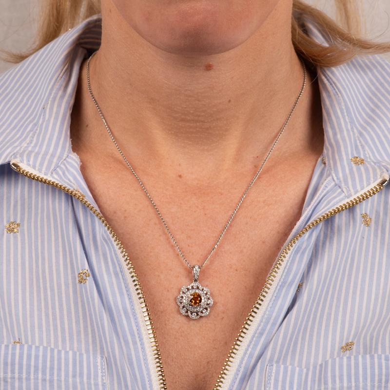 This pendant necklace features a 1.64 carat round Mandarin orange garnet surrounded by a floral halo of 1.04 carat total weight in round brilliant and princess cut diamonds set in 18 karat white gold. 
Measurements: 18