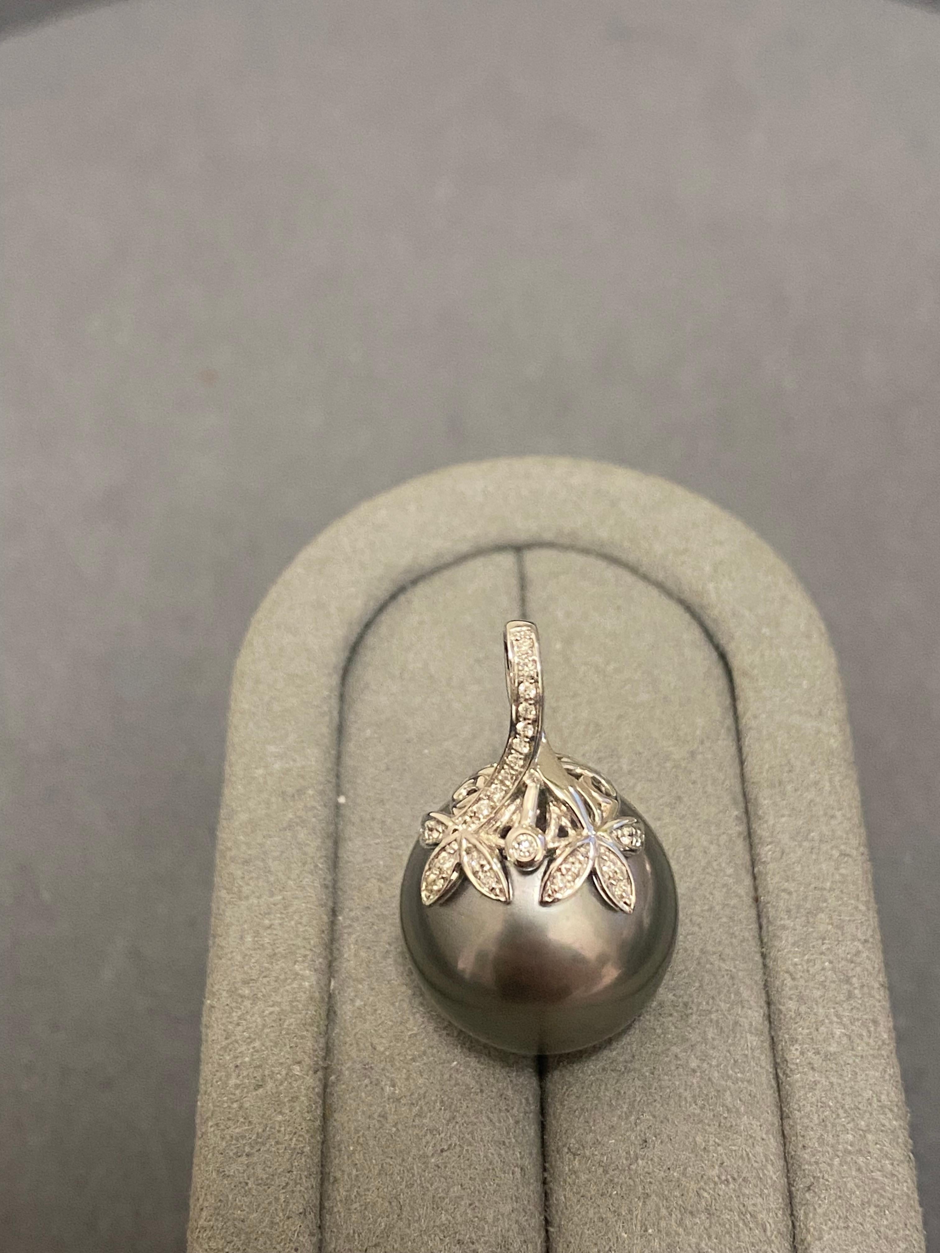A 16.4 mm grey colour Tahitian Pearl and diamond pendant in 18k white gold. The pearl pendant is in bale setting and the bale is encrusted in micro diamonds. The bale has a floral leaf-like design and there is a round diamond set in the middle of