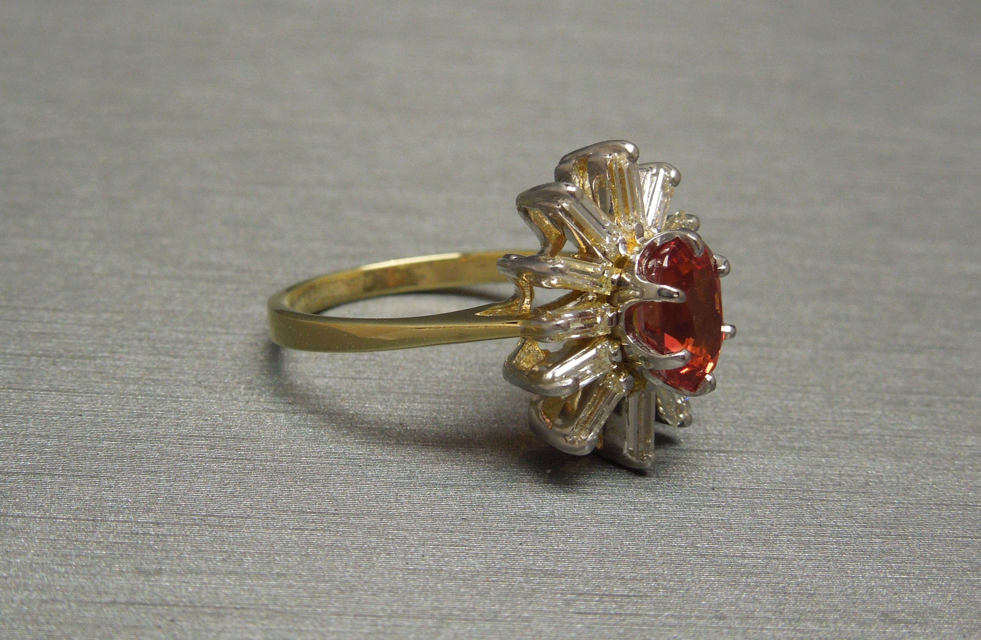 Containing 1 Central Bezel set 1.65 carat Oval cut Natural Padparadscha Sapphire solitaire at 7.7mm in length x 5.1mm in width securely set in a six-prong White Gold head with a total of 12 Nearly Colorless Nearly Flawless Rectangular Baguette cut