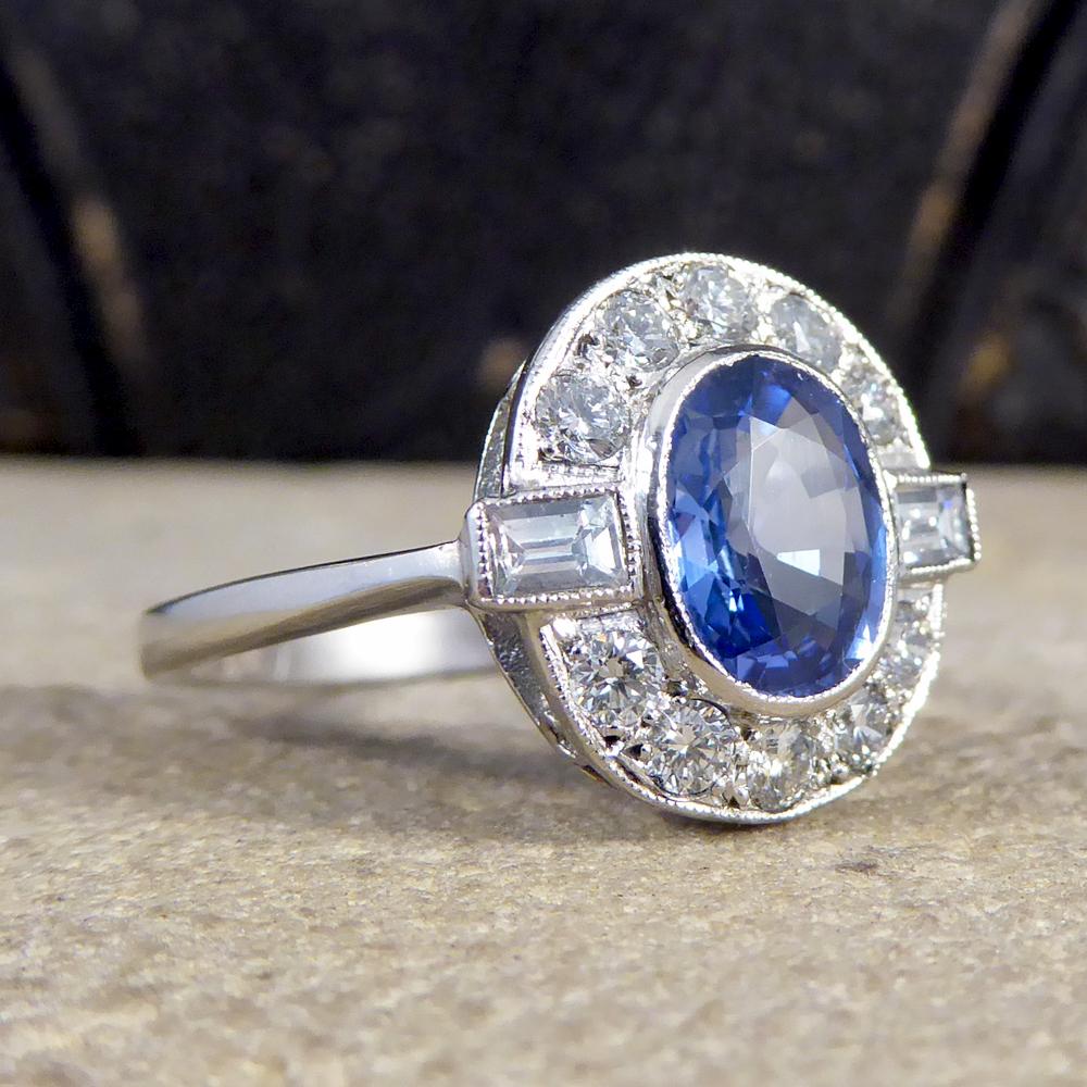 This captivating blue Sapphire weighs 1.65ct with a surround of Diamonds weighing 0.55ct in total of both modern brilliant cut and baguette cut Diamonds. All the gems are set in a rub over collar setting with a millegrain edge resembling an Art Deco