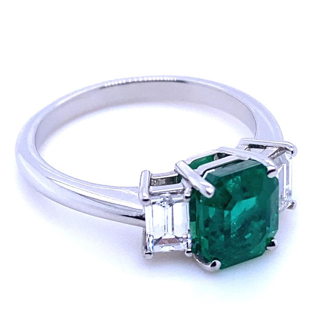 A 1.65 carat Zambian emerald and diamond three stone platinum engagement ring.

This beautiful emerald and diamond engagement ring is handcrafted in platinum. The piece is claw set to its centre with an exceptional emerald cut emerald of 1.65