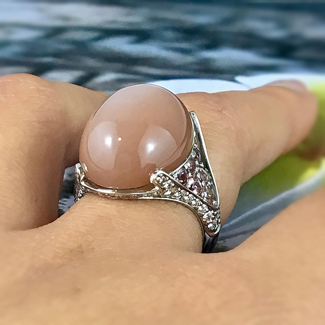 A fun cocktail ring showcasing a warm coloured rose moonstone contrasted by round soft pink tourmalines and round brillant diamonds on the shoulders. The Moonstone weighs 16.54 carats. The diamonds have a total weight of 0.66 carat, Colour G,
