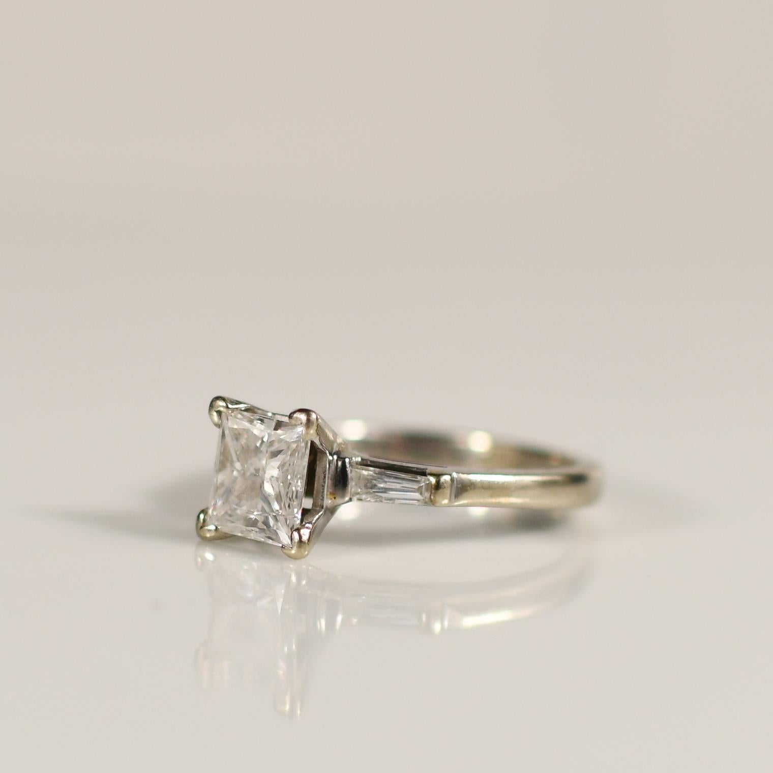 Experience unparalleled brilliance with this exquisite 14K white gold ring showcasing a dazzling 1.4 carat princess cut diamond flanked by tapered baguette diamonds. The combination of geometric precision and sparkling accents creates a stunning