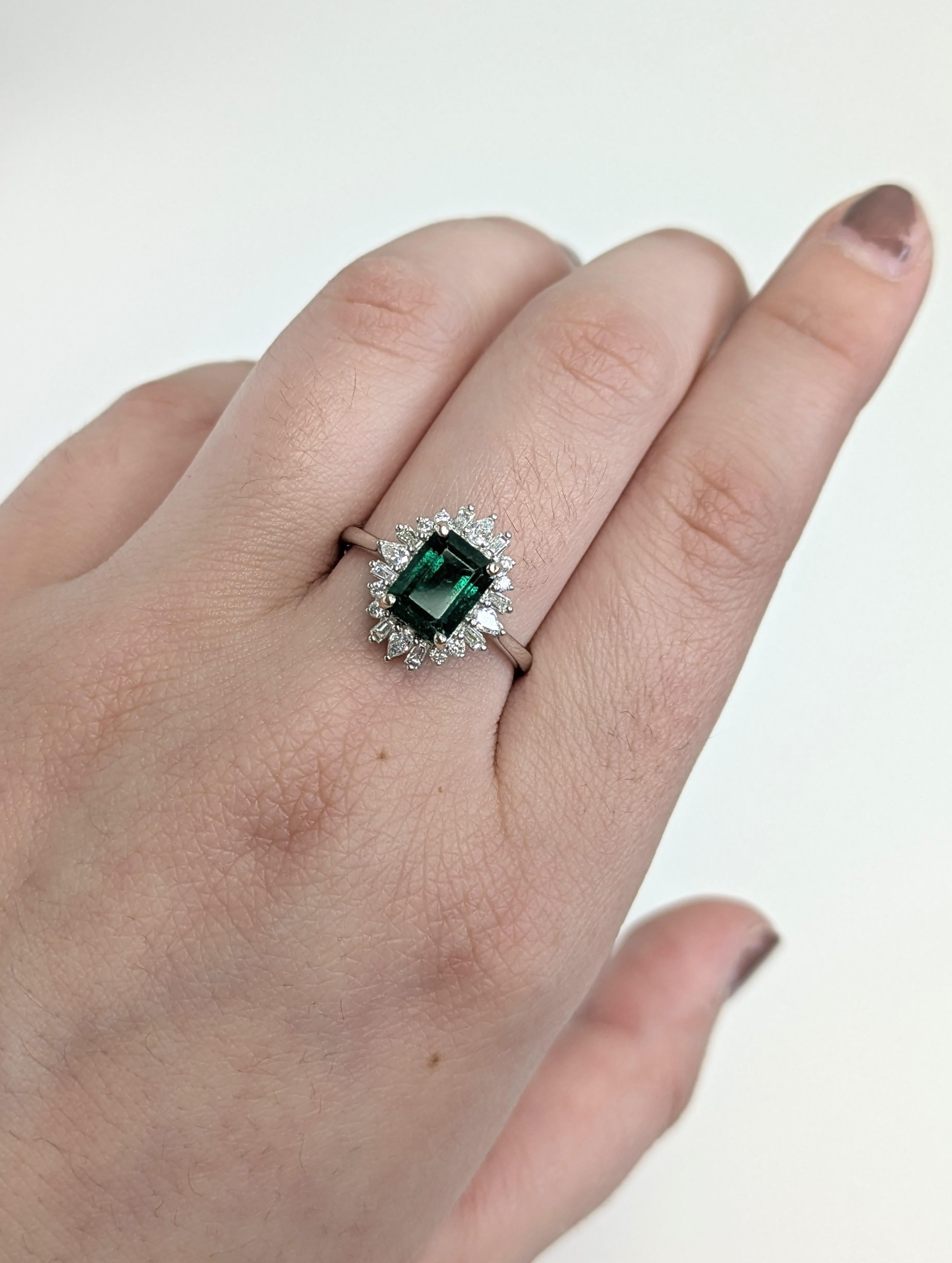 Dieser atemberaubende Ring zeigt einen 1,66-karätigen sambischen Smaragd, der von einem strahlenden Halo aus Diamanten in verschiedenen Formen umgeben ist. Der aus massivem 14-karätigem Echtgold gefertigte Anhänger verbindet zeitlose Eleganz mit