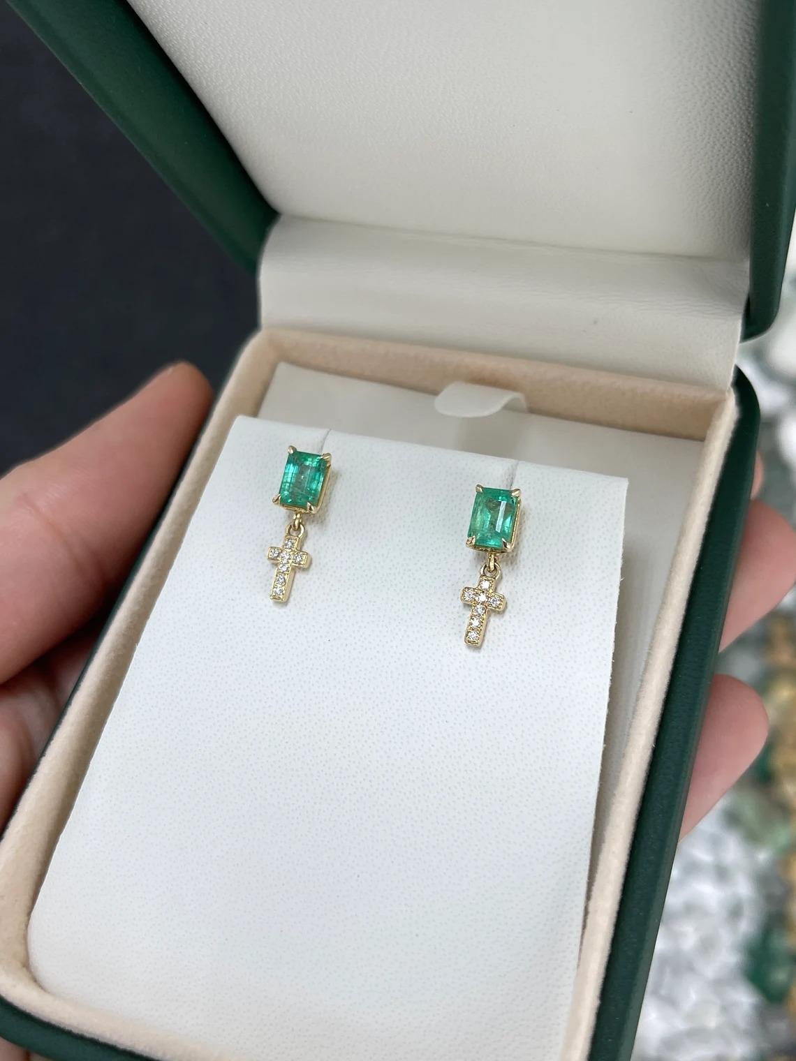 These exquisite emerald and diamond cross earrings feature natural emeralds with a lush green color, stunning emerald cut, and good clarity and luster. The emeralds are securely prong-set, serving as the radiant studs. Below the emerald studs,