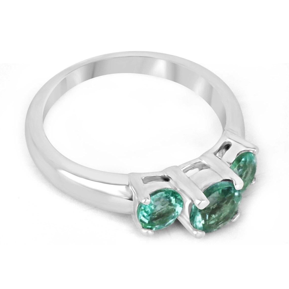 This emerald three-stone ring showcases a trio of round-cut emeralds, each possessing a captivating medium-green hue with remarkable characteristics. The emeralds exhibit eye-clean clarity and boast excellent luster, creating a mesmerizing display