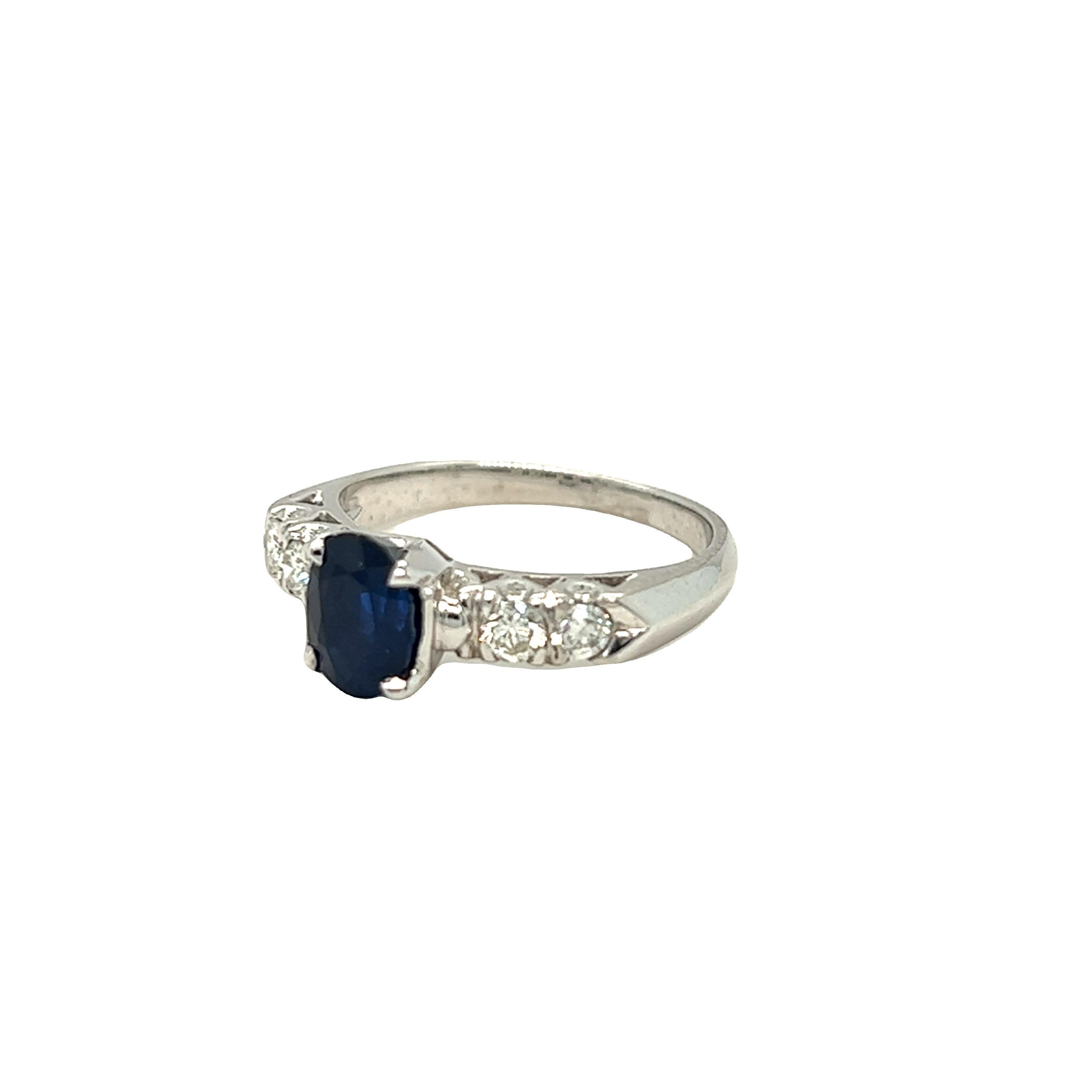 A tailored and very wearable sapphire and diamond ring centering a rich, deep blue 1.66 carat oval sapphire highlighted on either side by two round brilliant diamonds. Mounted in 18k white gold. The ring is currently in a size 6 and may be resized.