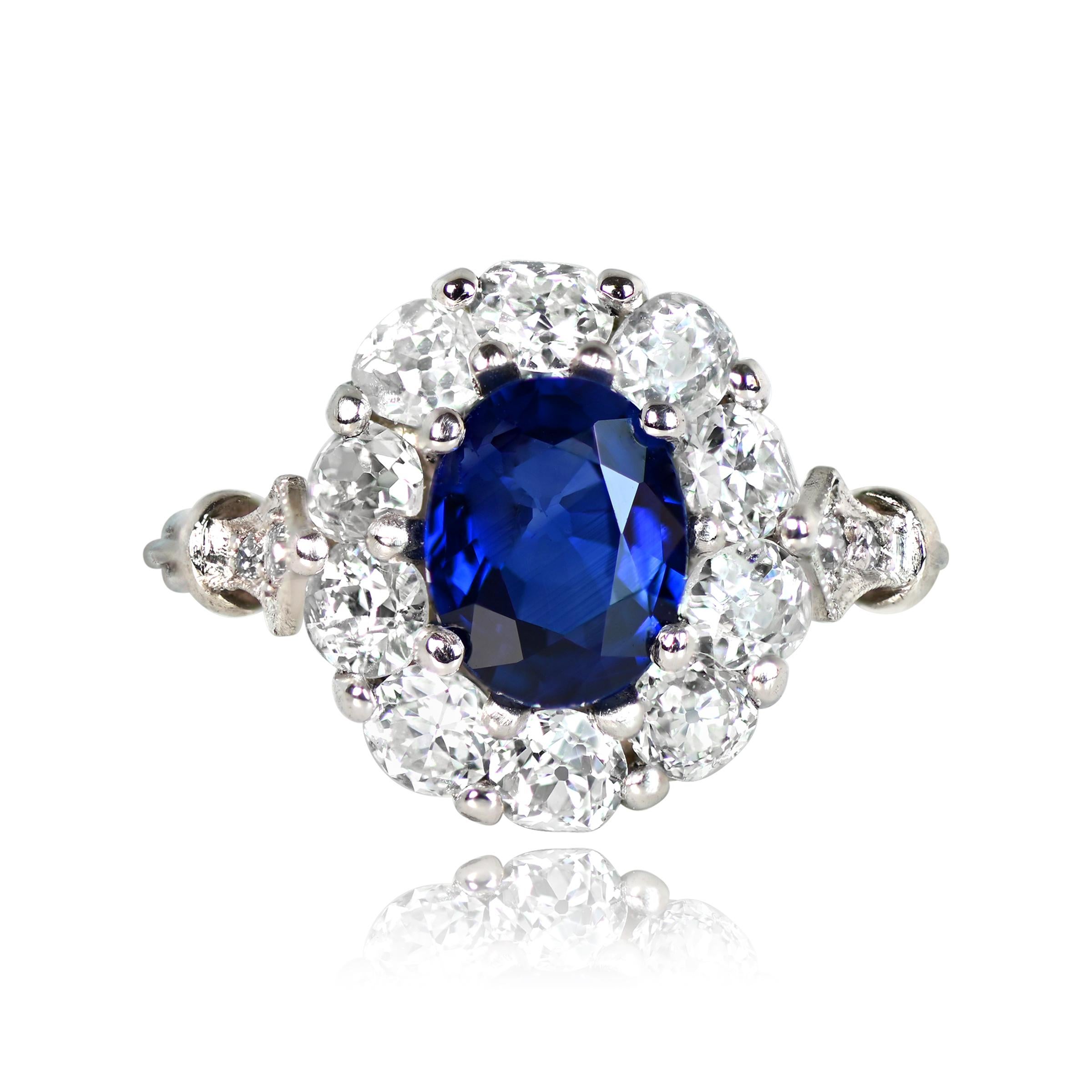 An exquisite cluster ring with a vibrant 1.66-carat natural blue oval cut sapphire at its center. The sapphire is encircled by a diamond halo in a floral arrangement. Ten old European cut diamonds, totaling around 1.00 carat, form the surrounding