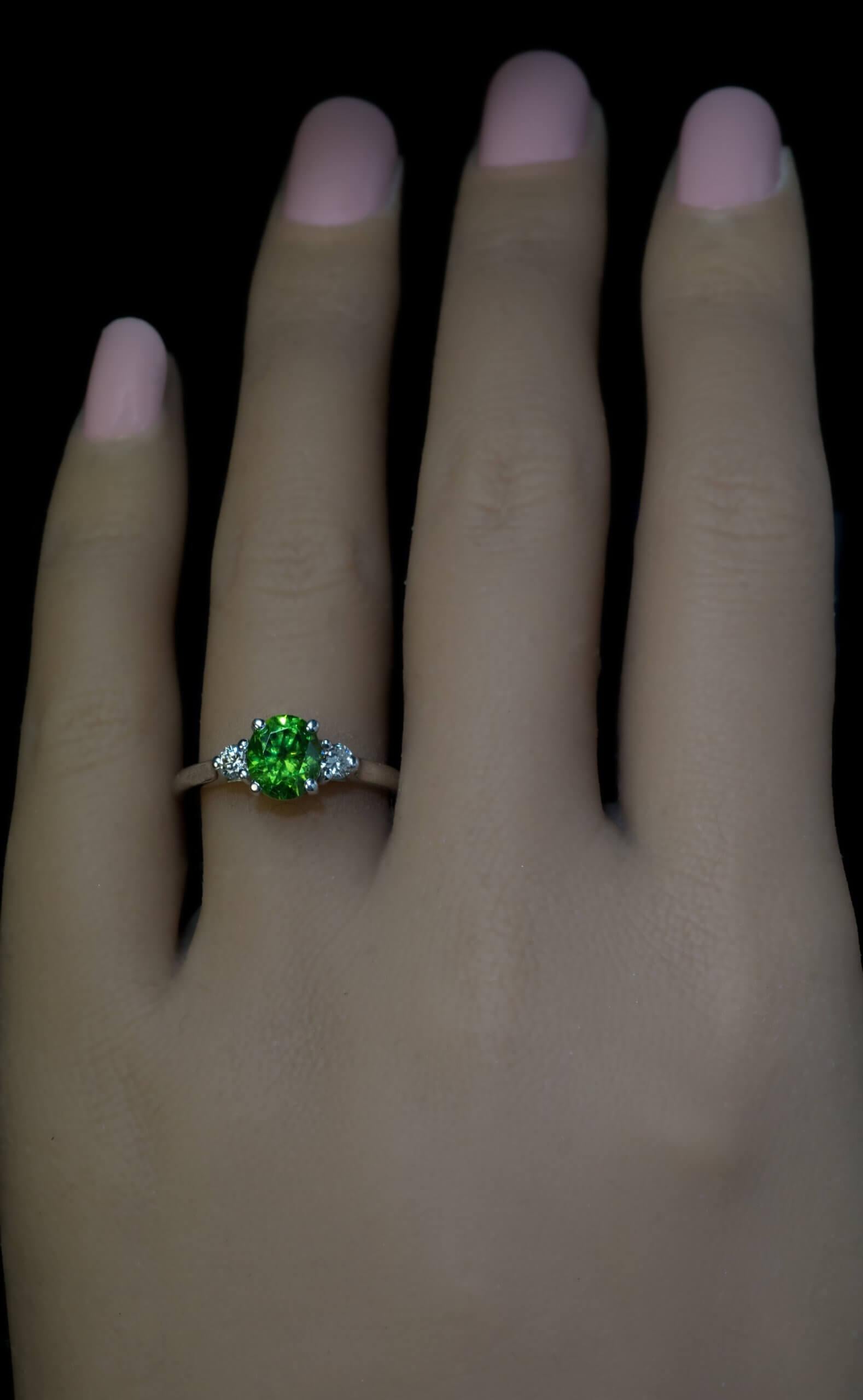 This contemporary custom-made 18K white gold ring features an oval 1.69 ct Russian demantoid (7.4 x 6.3 x 4.7 mm) of excellent golden green color. The demantoid is flanked by two bright white diamonds ( 0.20 ct total weight, F-G color, VS-SI