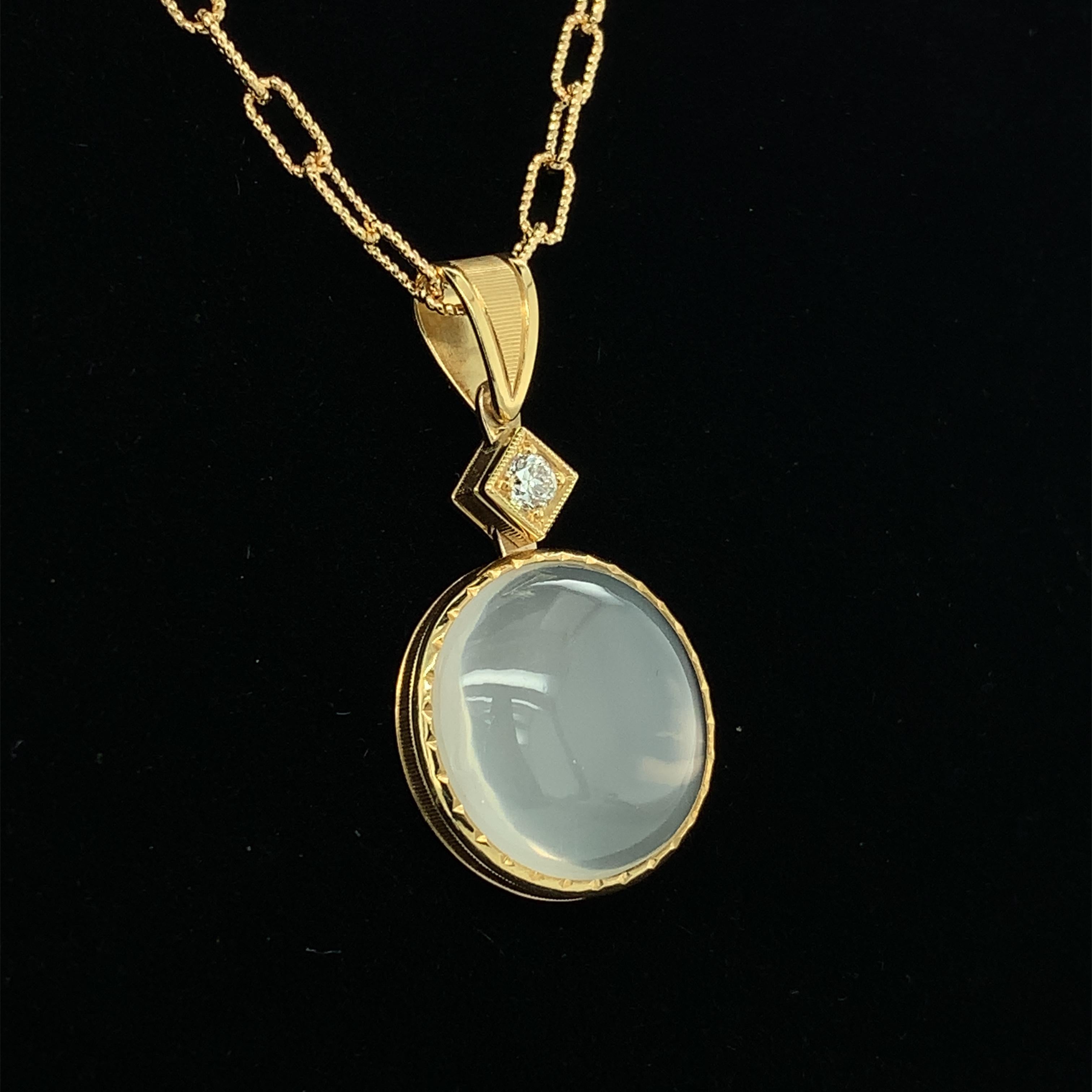This striking pendant features a large and impressive round moonstone set in an exquisite 18k yellow gold handcrafted and hand engraved bezel. Set atop the moonstone drop is a beautiful round diamond in its own handmade setting. The workmanship on
