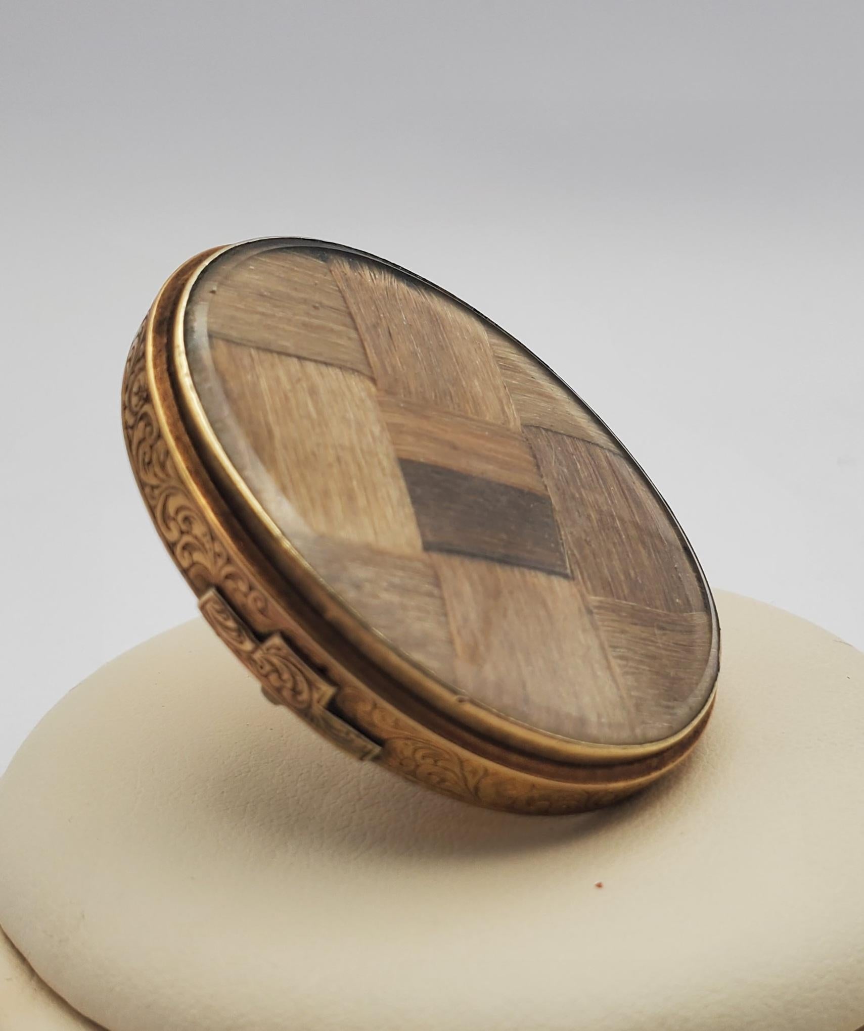 Beautiful and large example of unique Victorian hair art In a mourning brooch. The pin features dark blond/light brown hair in a basketweave design behind a glass protective plate. The back side of the brooch features a smaller window showcasing an