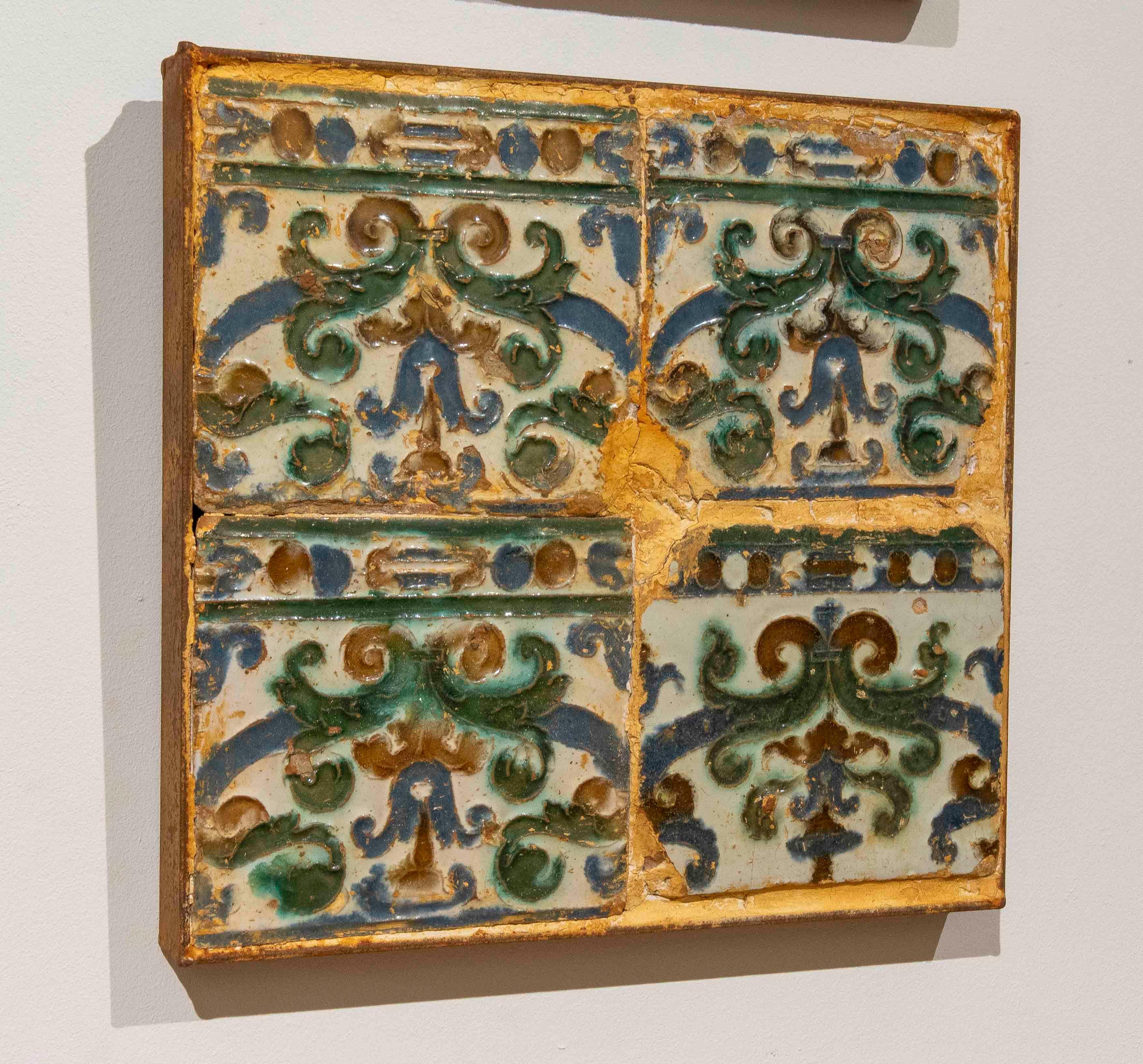 Panel composed of four antique tiles decorated with plant reliefs in shades of green, blue, and brown on a light background. Made using the cuerda seca technique, they exhibit patina, crackling, and wear that enhance their historical and artisanal
