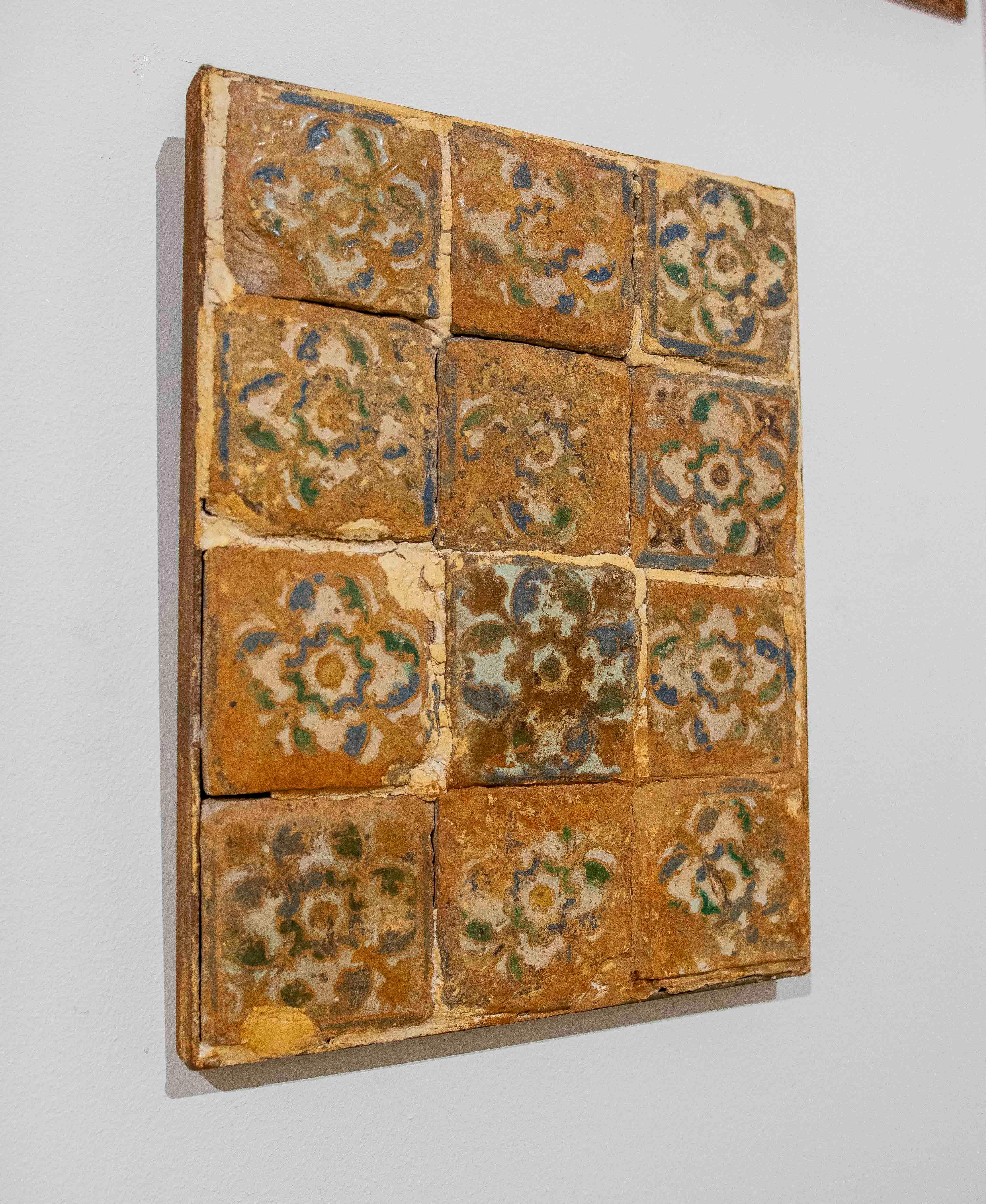 Panel composed of twelve antique 16th-century tiles, decorated with floral motifs in soft shades of green, blue, and brown. Each piece displays patina, wear, and crazing characteristic of its age, lending it great authenticity and handcrafted charm.