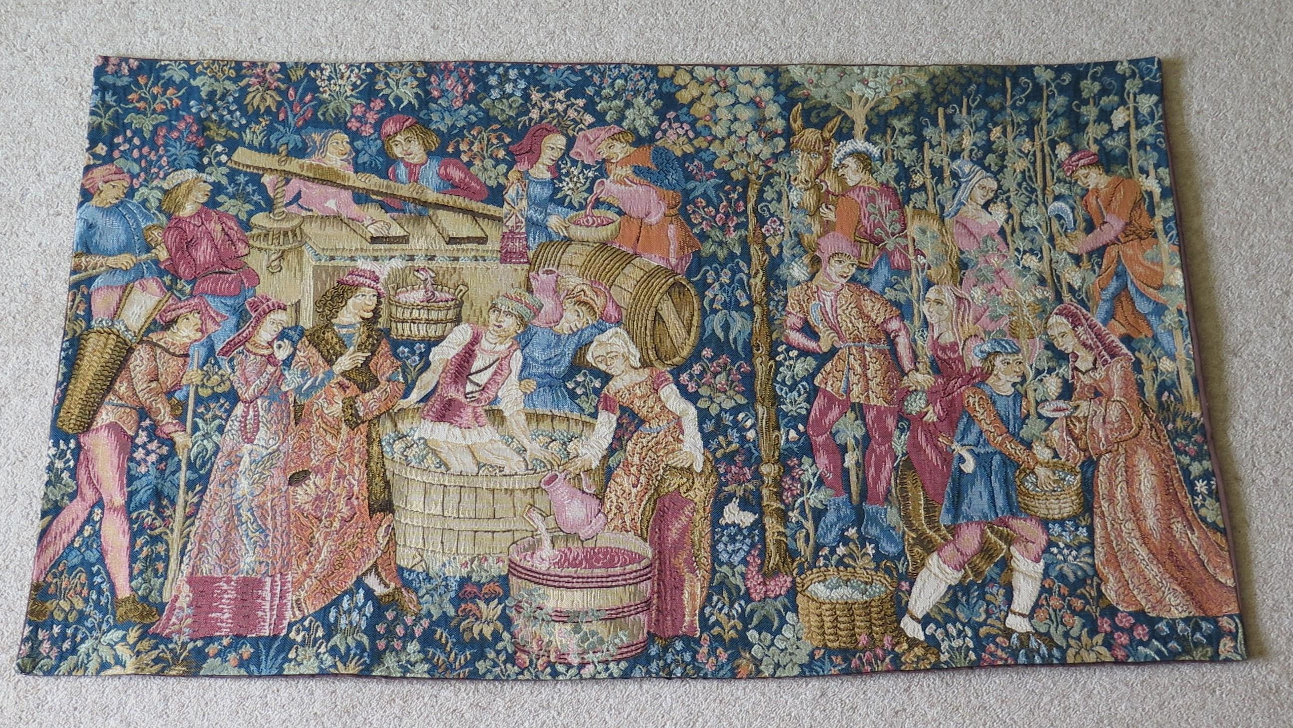 This is a 16th century style inspired French or Flemish woven, wall-hanging, tapestry depicting a wine making and grape harvesting scene in a country setting, with village folk and nobles surrounded by trees, shrubs and woodland