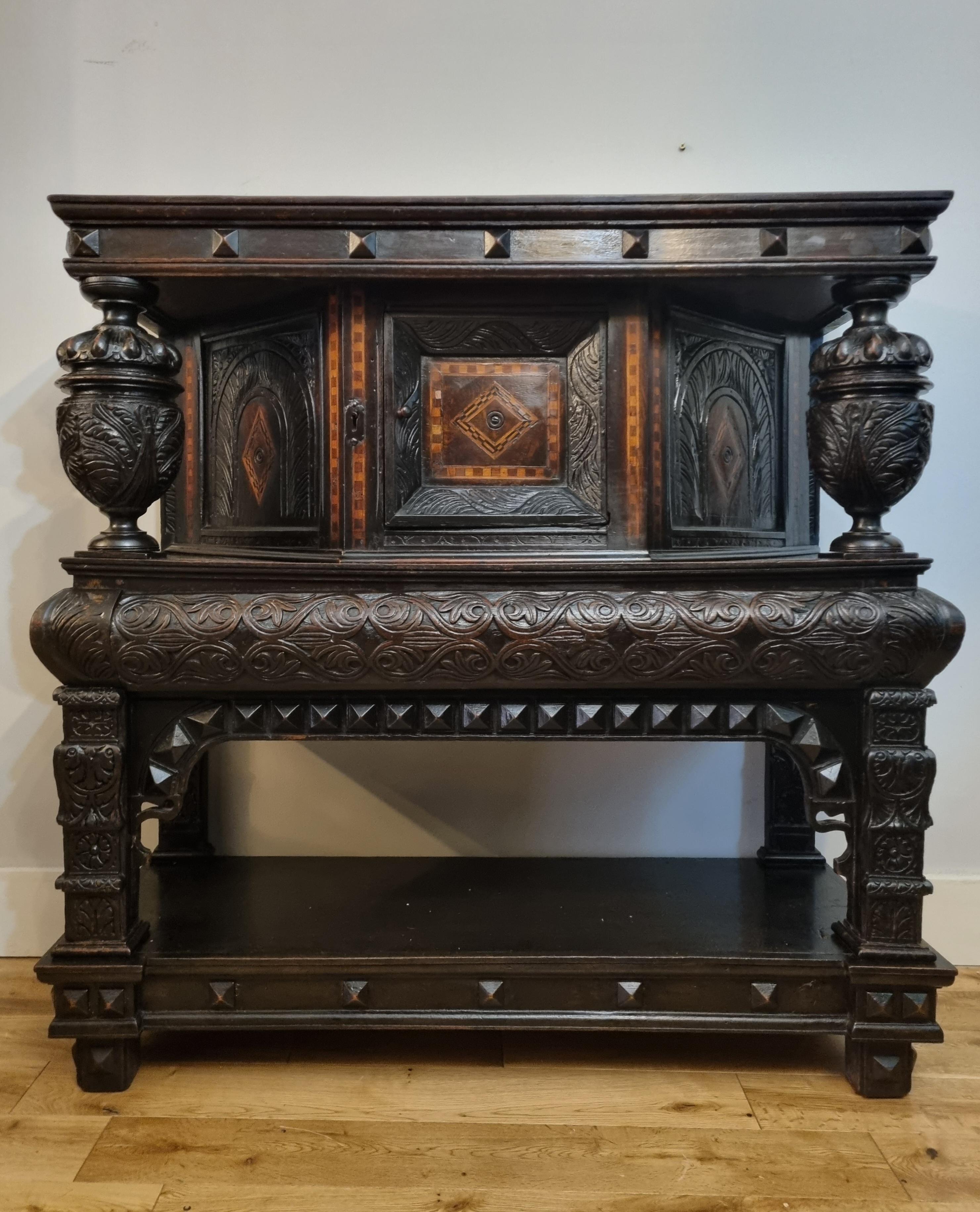 A superb Elizabethan inlaid oak livery cupboard, dating to 1570-1590, of desirable small proportions. An extremely rare example, beautifully carved and featuring intricate inlay work, geometric arch moulding, wonderfully carved cup and cover