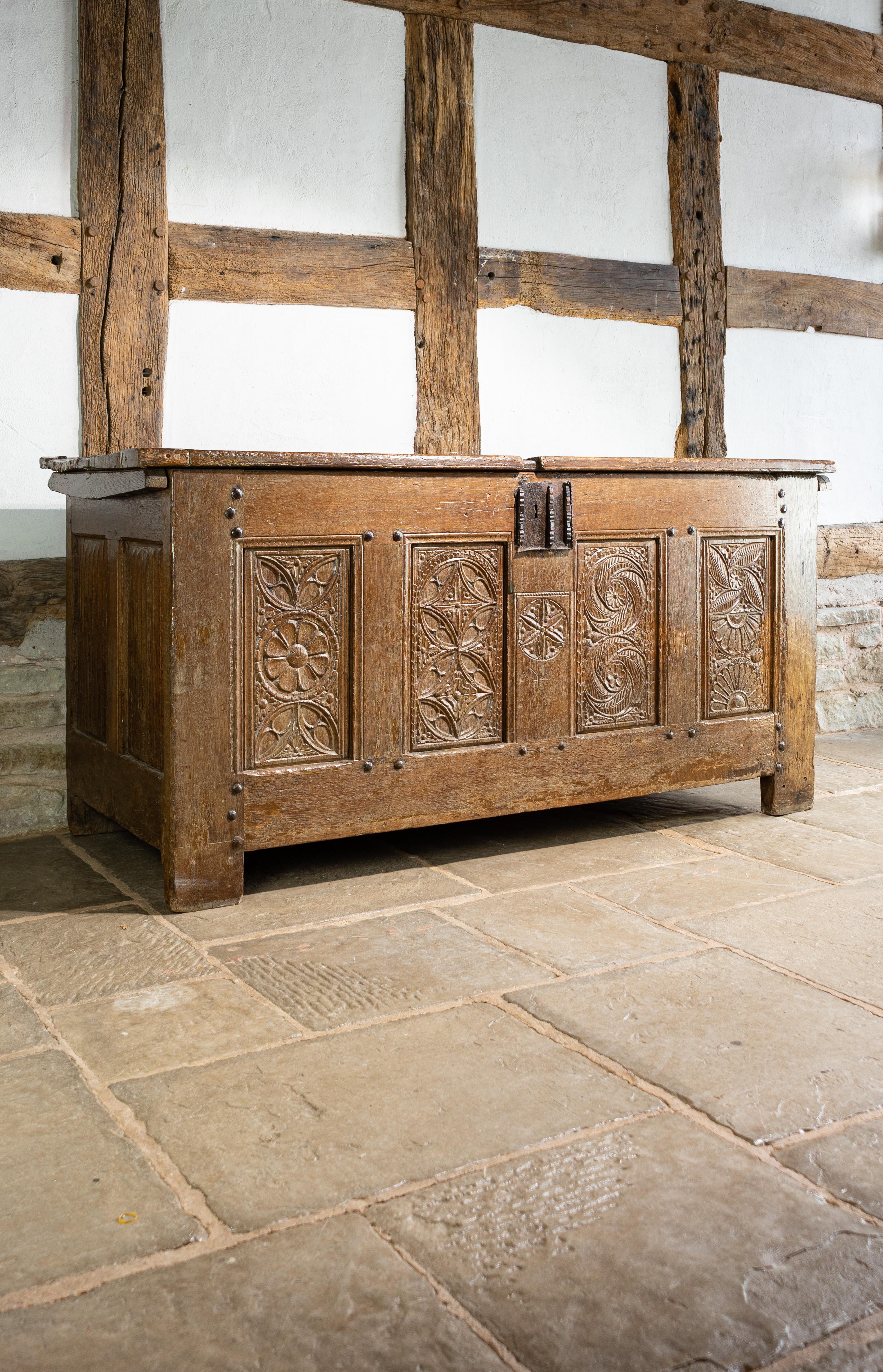 An impressive early 16th Century oak coffer, Normandy, circa 1500, having a deep plank hinged top, above a series of four Gothic tracery carved panels, each of different design within broad mason’s mitred rails, the muntin rail below the iron