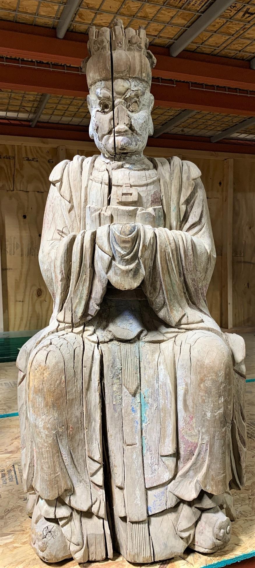 Remarkable 16th century Ming dynasty hand carved wood sculpture of a Buddhist deity donning a crown and dressed in loose robe with heavy folds about the legs, arms, and body. Retains traces of color pigment. The piece is now mounted to a museum