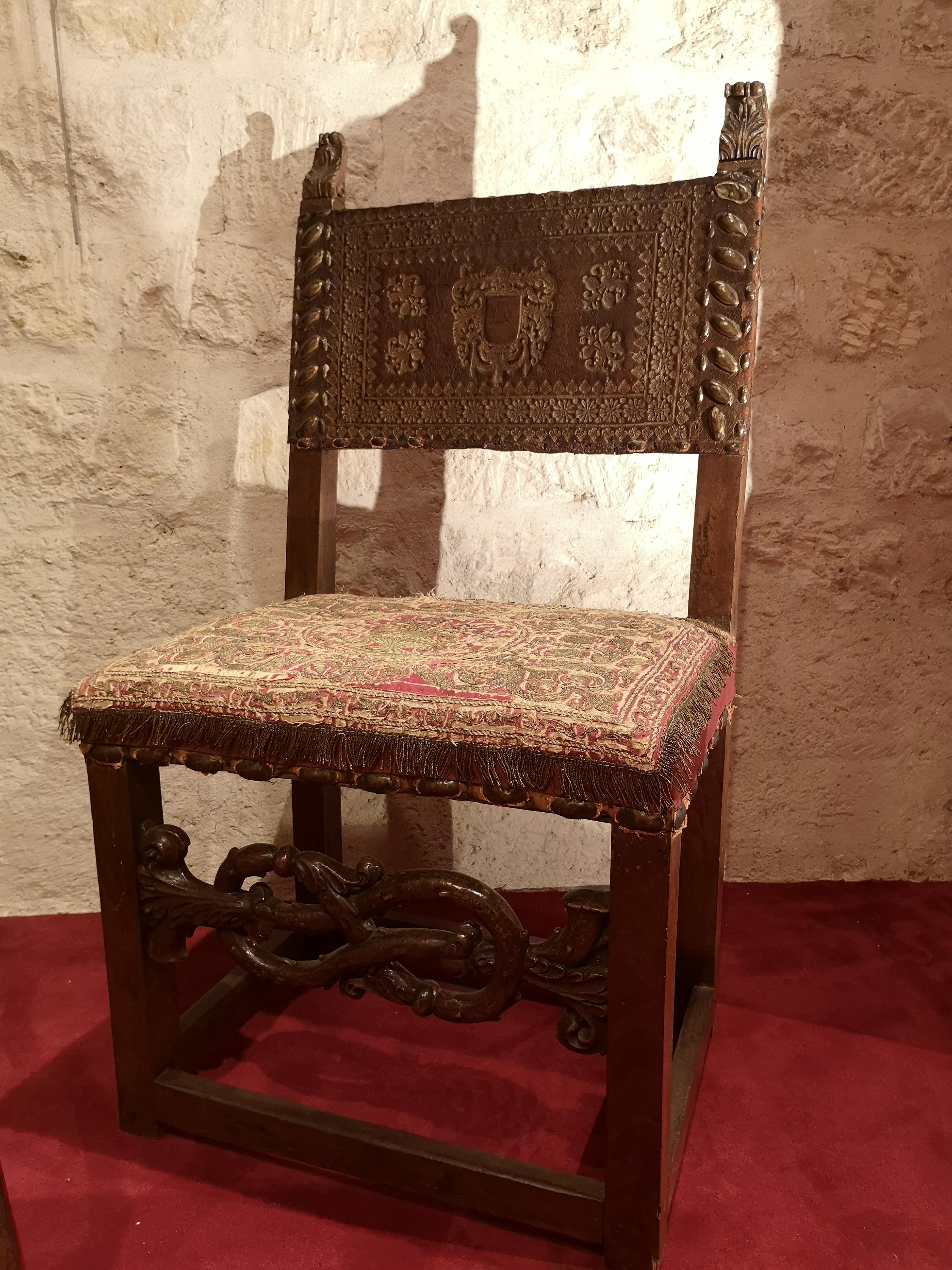 This walnut chair stands on four square-section feet linked by four crossbars. The front spacer is carved as an intertwined branch. The backrest’s jambs are adorned with leaves motifs. The chair is upholstered with embossed and gilt leather secured