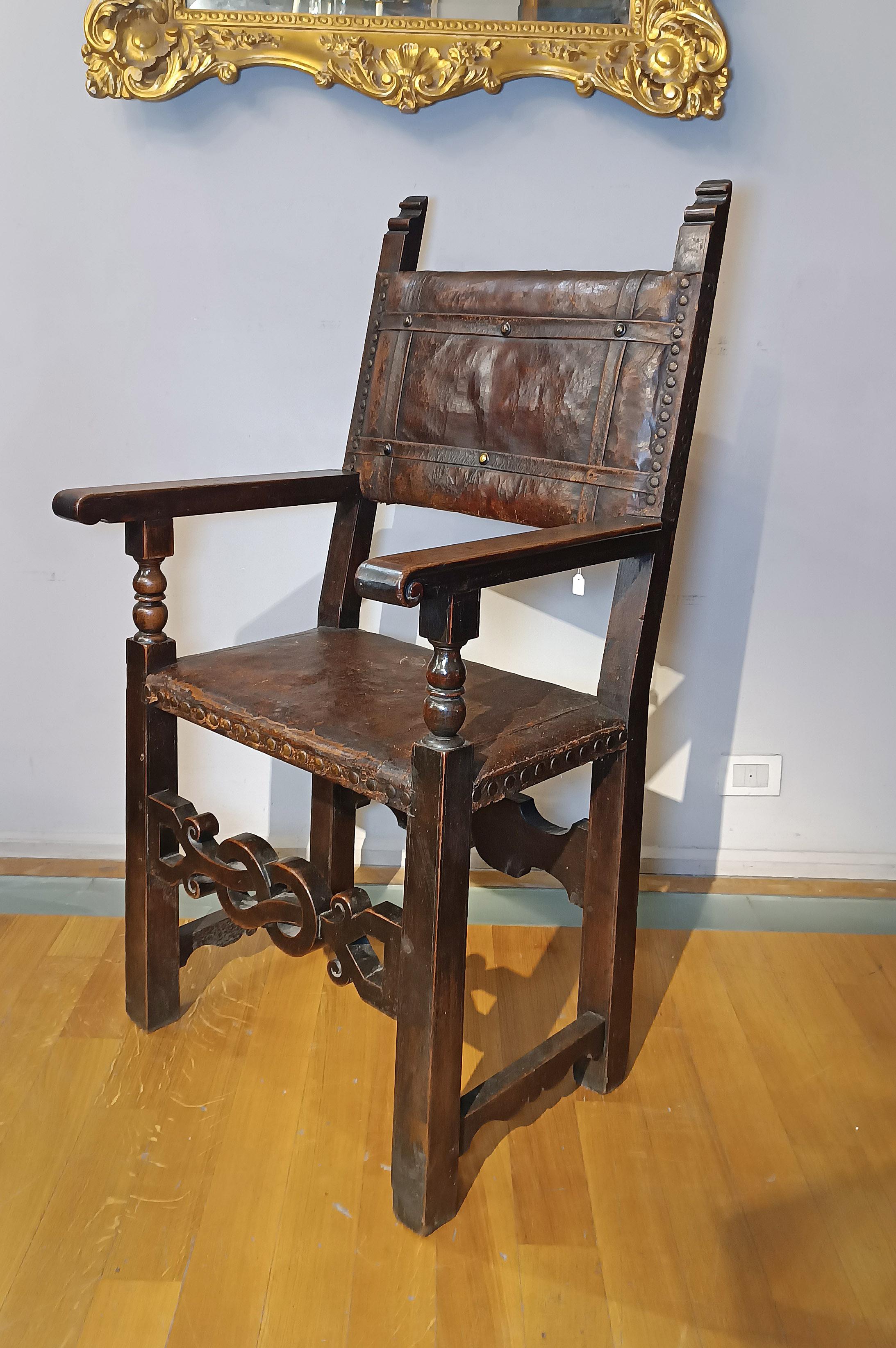 Elegant armchair in carved solid walnut, enriched with original leather parts on the back and seat. This chair, emblematically representative of the Tuscan Renaissance tradition, has straight legs and armrests, while the under armrest is finely
